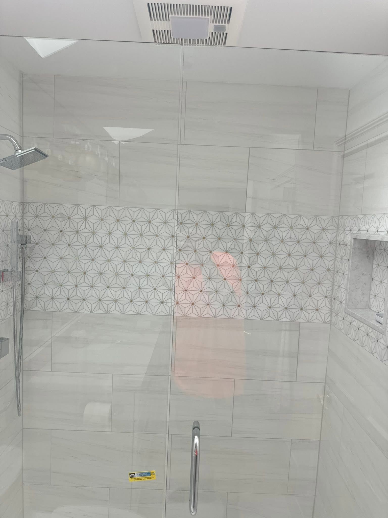 Modern shower stall with white tiles, a gray mosaic accent band, and a glass door handle