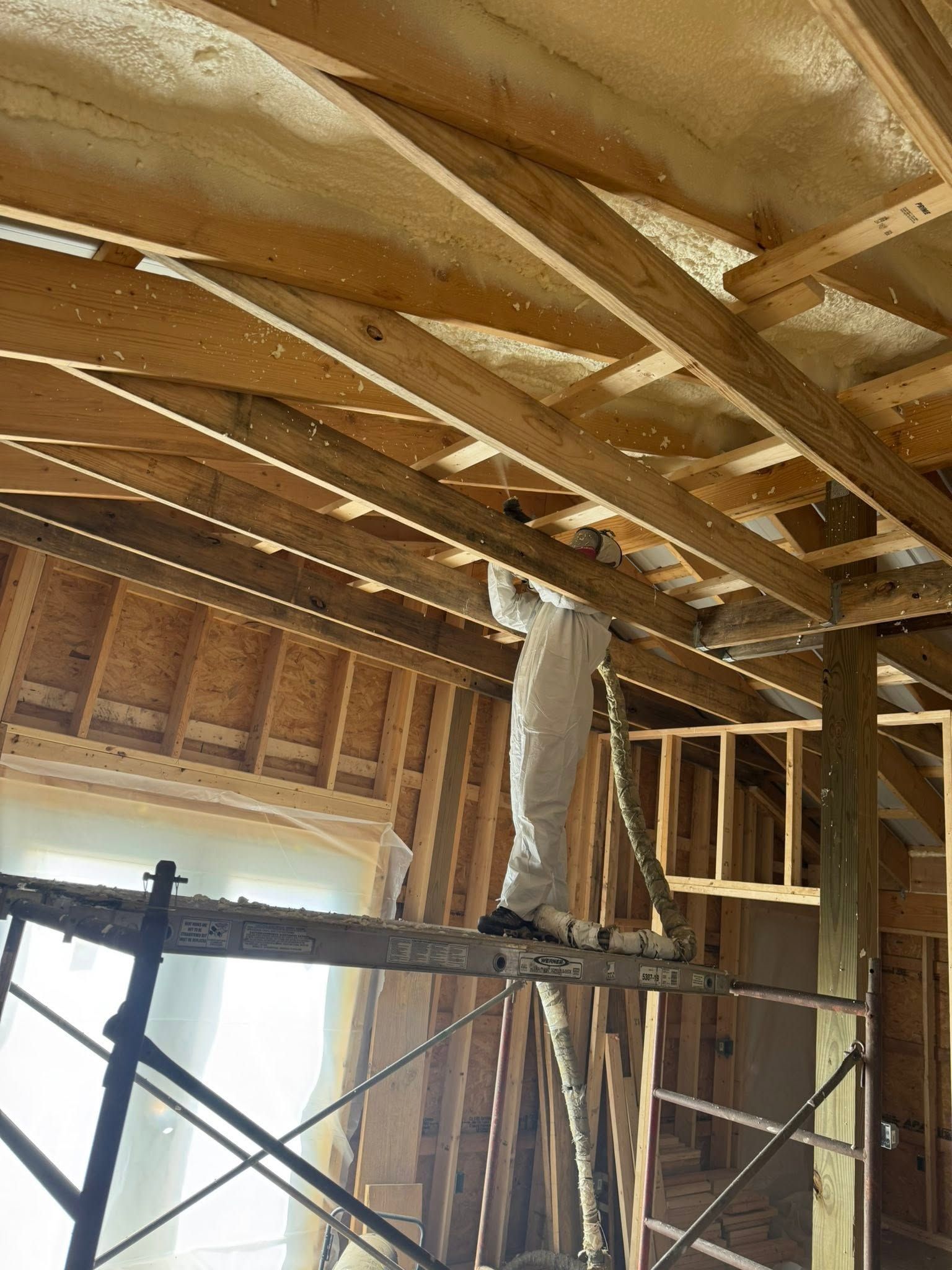 Interior of a house under construction with exposed roof framing, scaffolding, and unfinished wood walls.