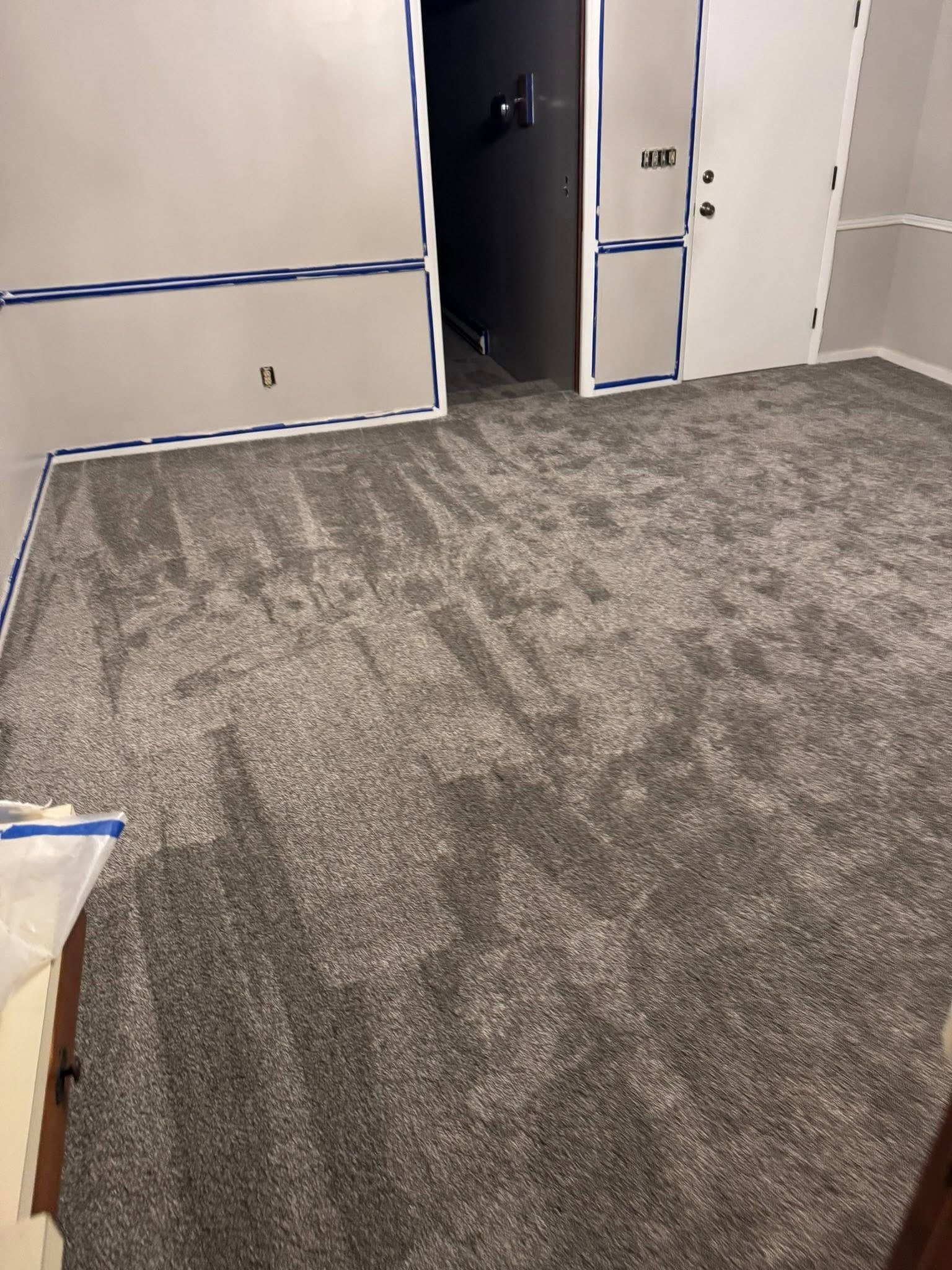 Empty carpeted room with beige walls and a doorway opening to a dark hallway