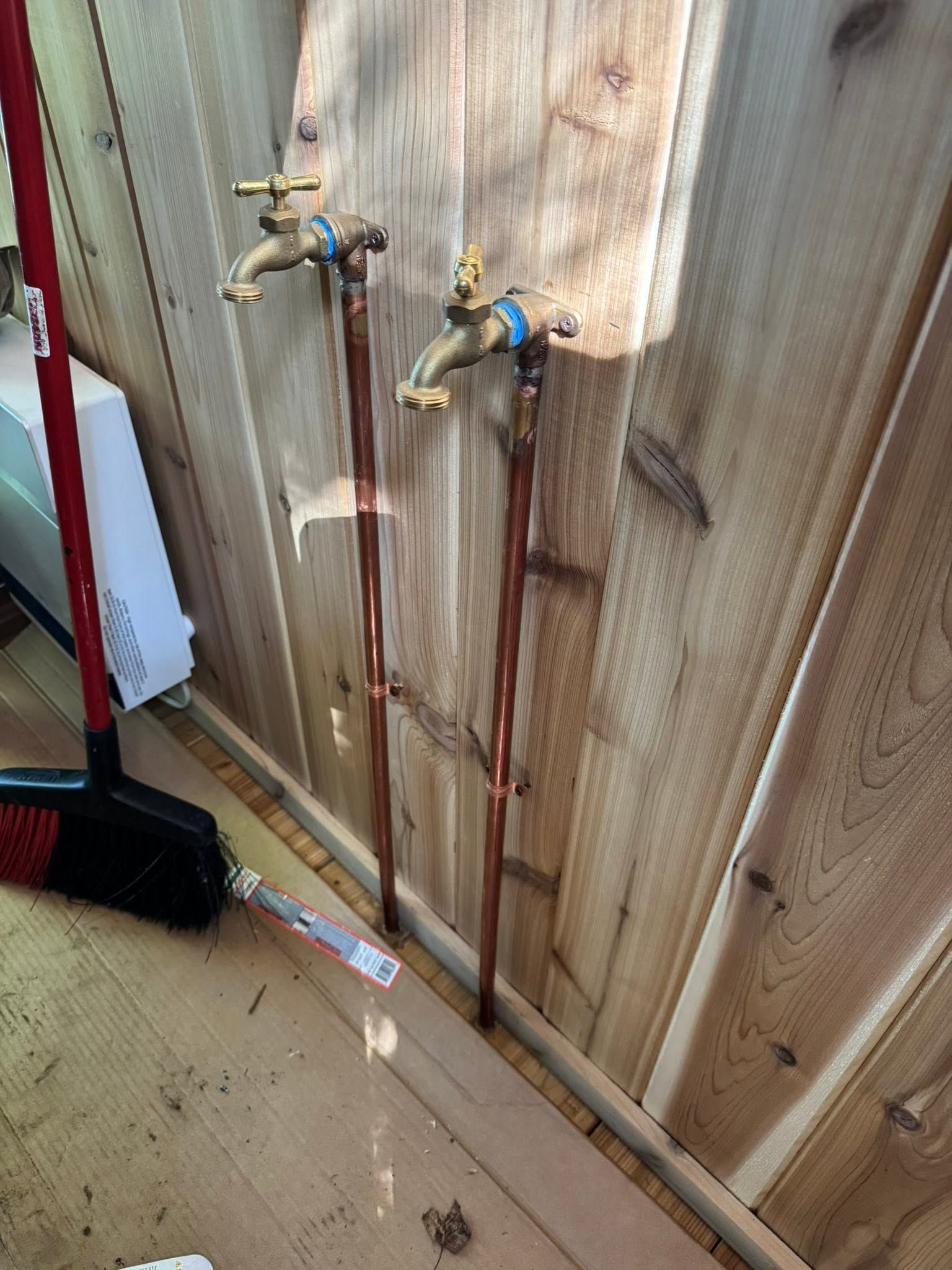 Two outdoor water faucets on a corrugated wall with rusty water streaks below them.