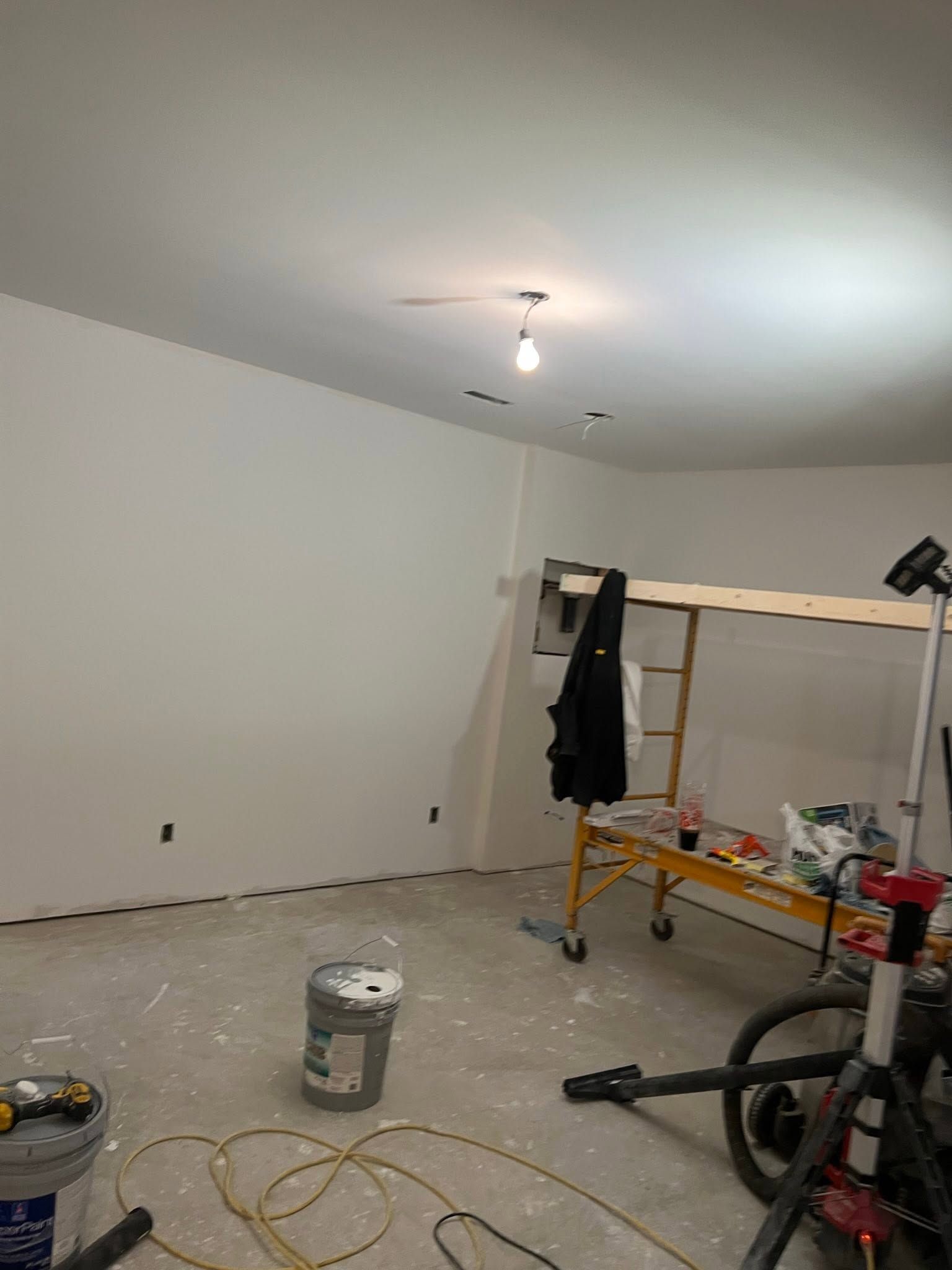 Empty room under renovation with ladder, paint bucket, and tools on the floor