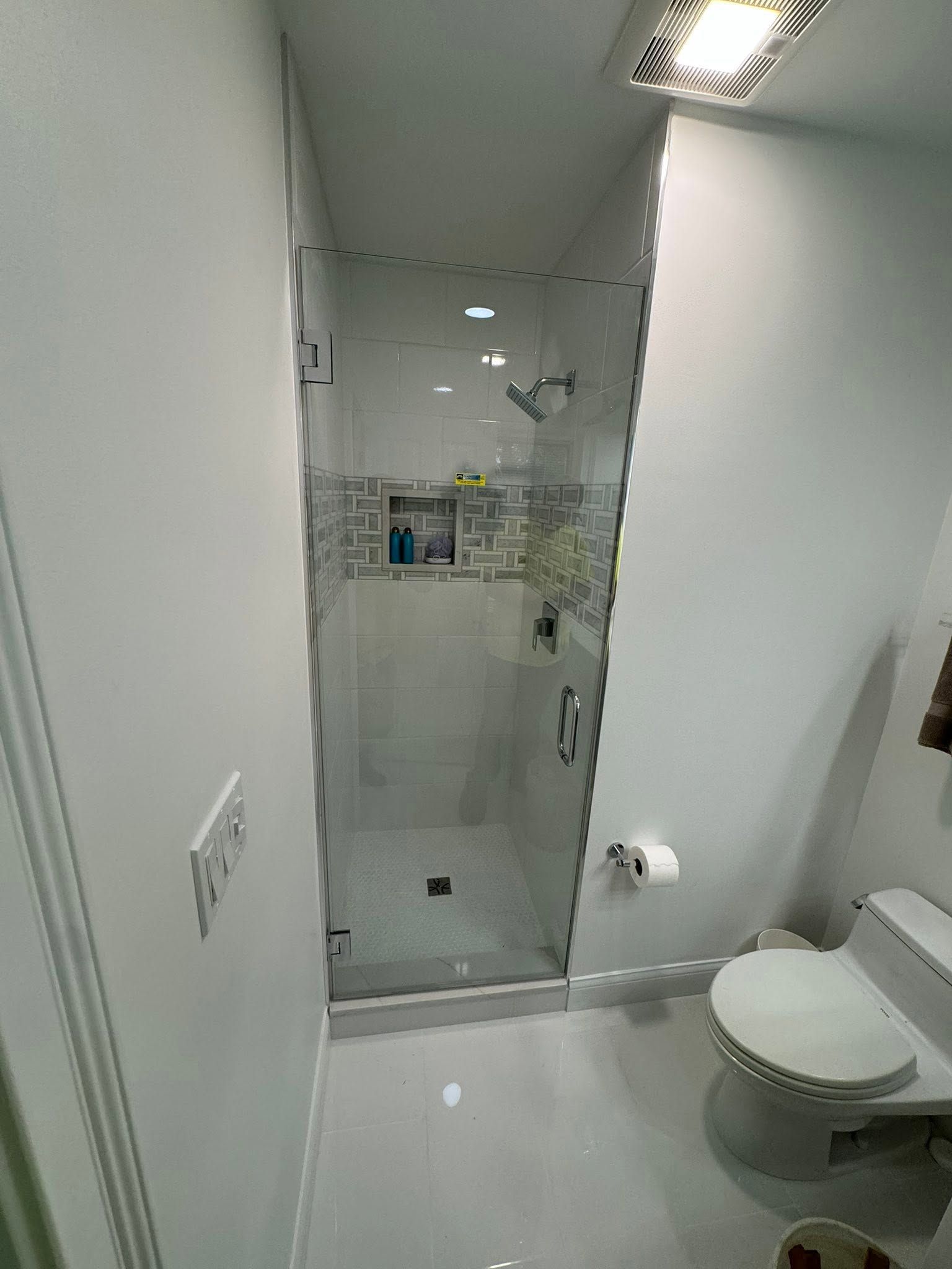Small bathroom with glass shower enclosure and toilet, in white and gray tones.