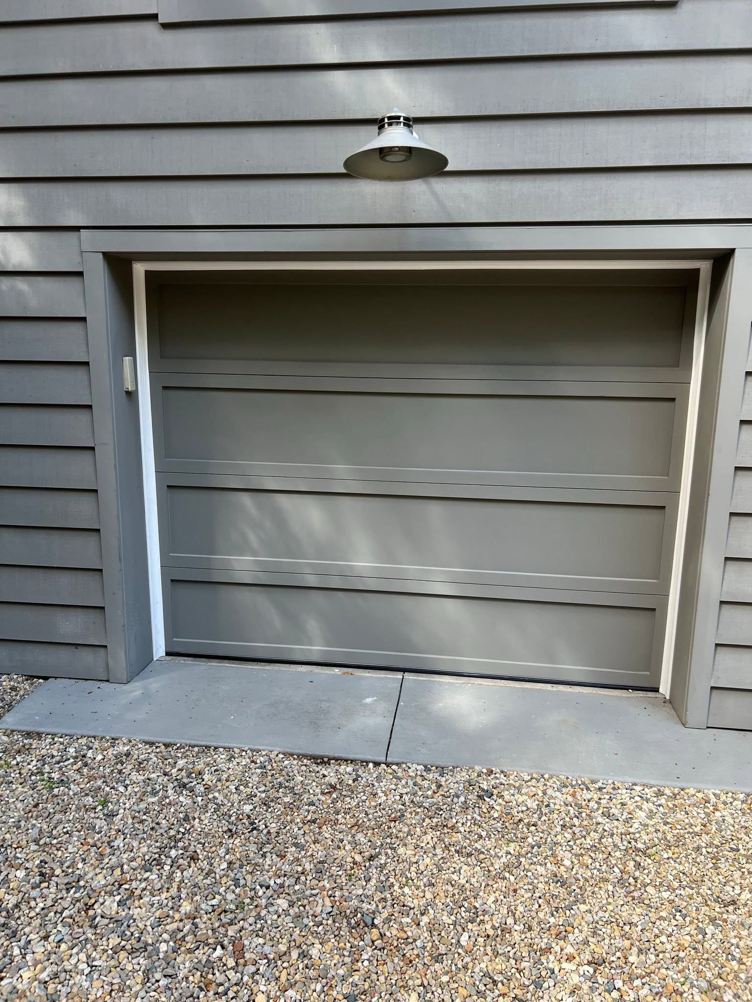 Garage door on a gray house with horizontal siding and a gravel driveway.