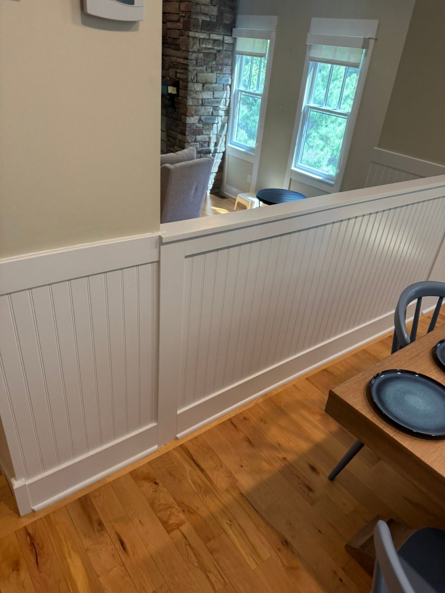 White beadboard half-wall in a bright dining area with hardwood floor and blue chairs near windows