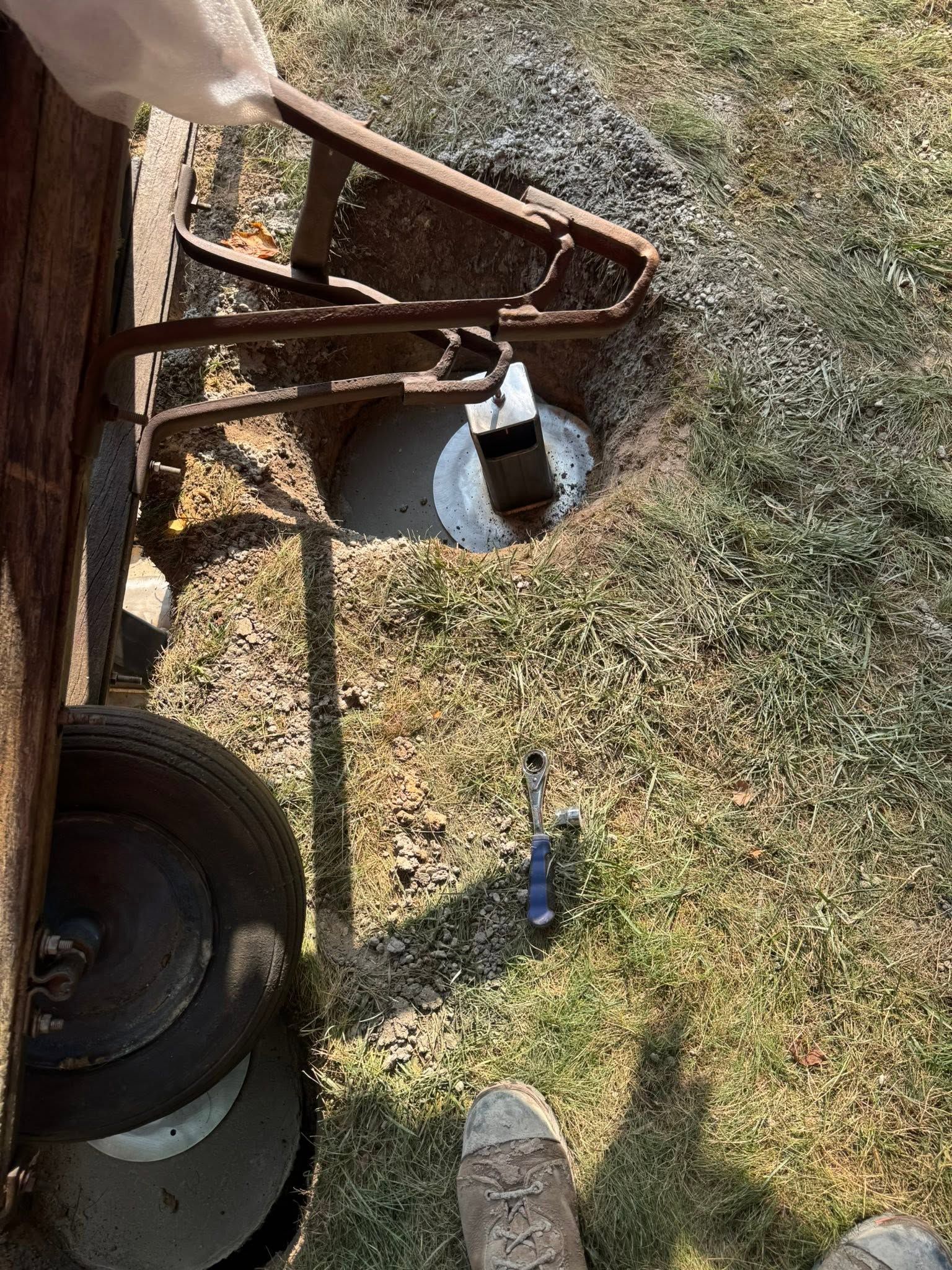 Hand pushing a rusted metal cart wheel in dry grass outdoors