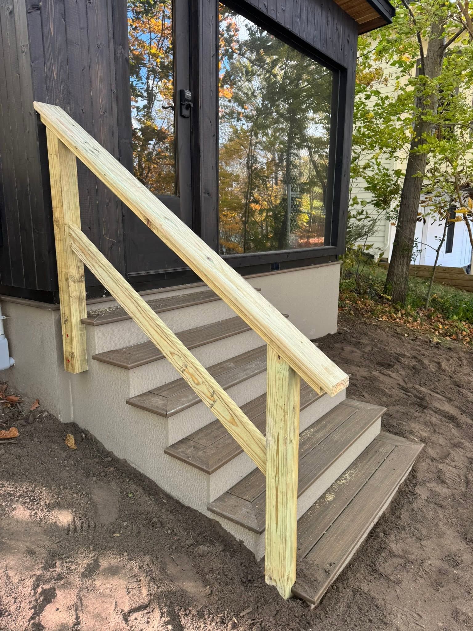 Concrete steps with a pale yellow wooden handrail beside a dark building in a wooded outdoor area