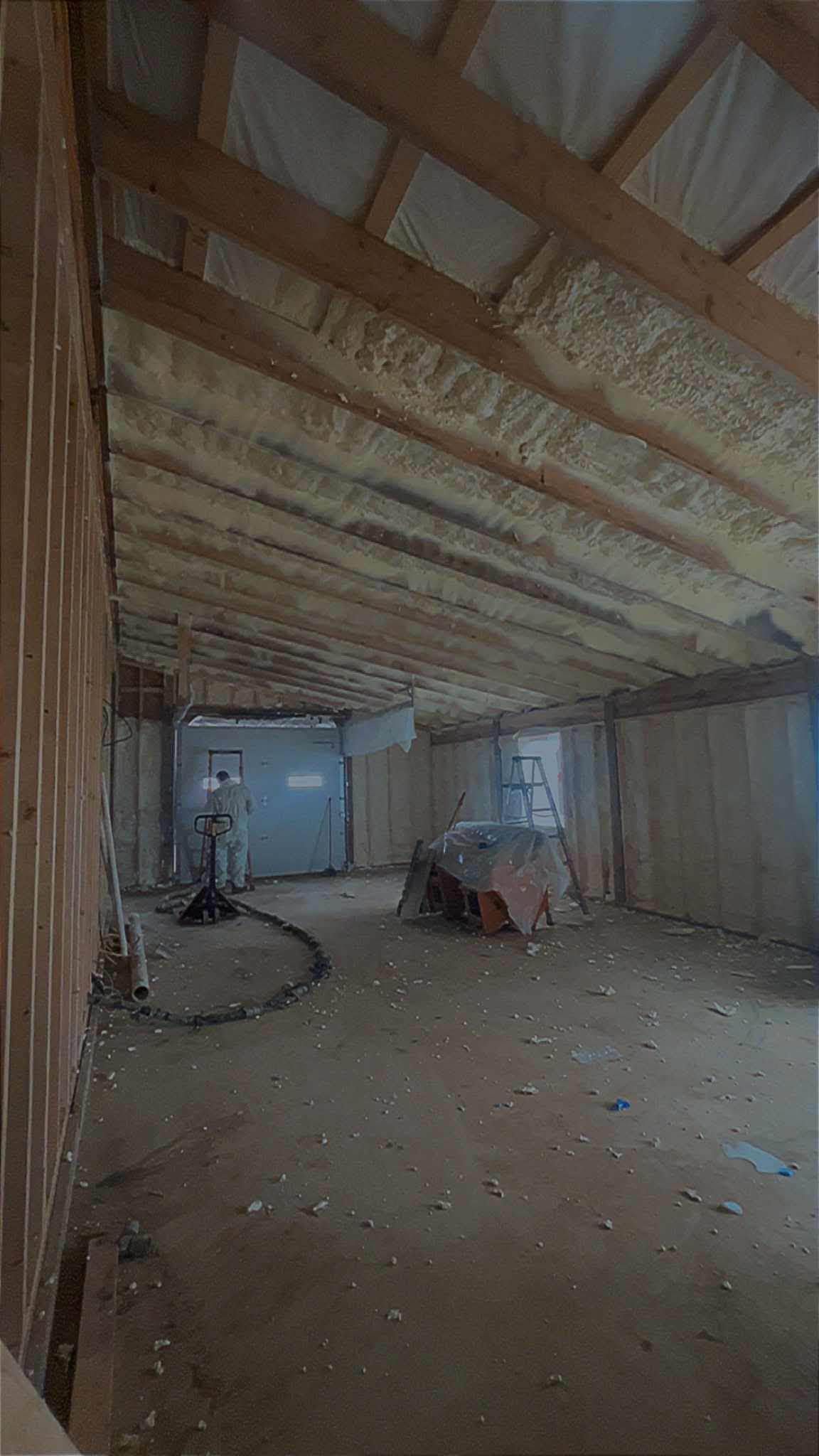 Interior of an unfinished room with exposed wooden beams, bare walls, scattered debris, and a small machine on the floor