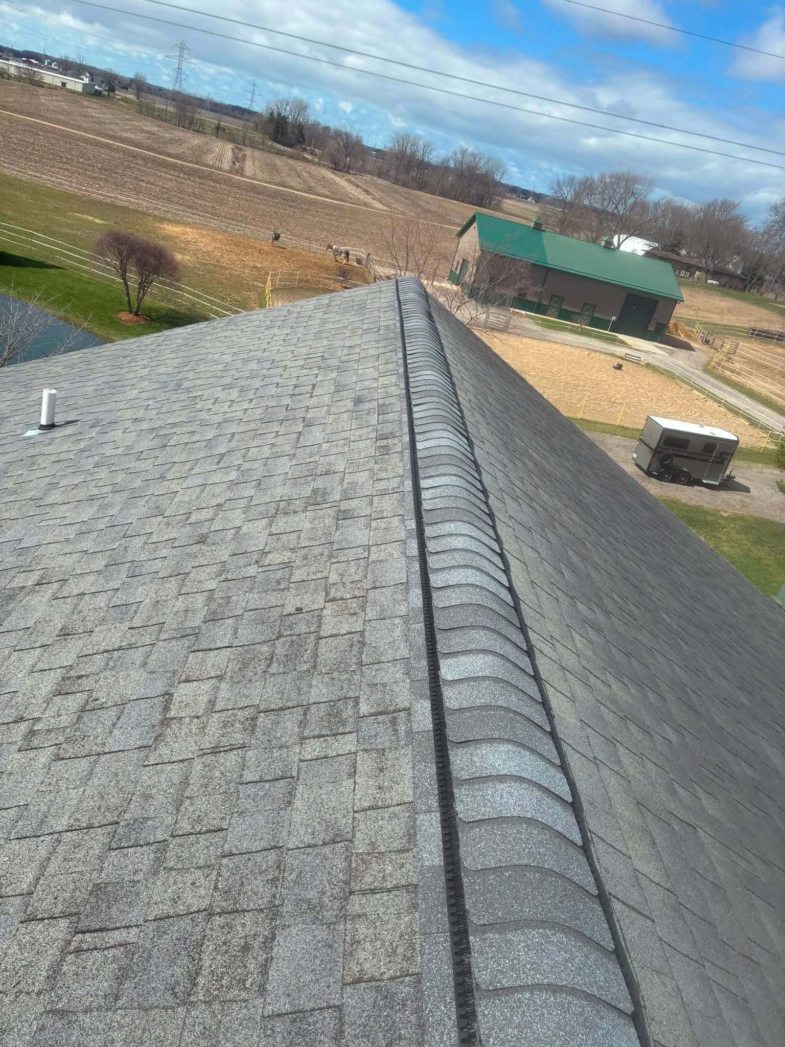 Gray shingled roof ridge overlooking farmland under a blue sky