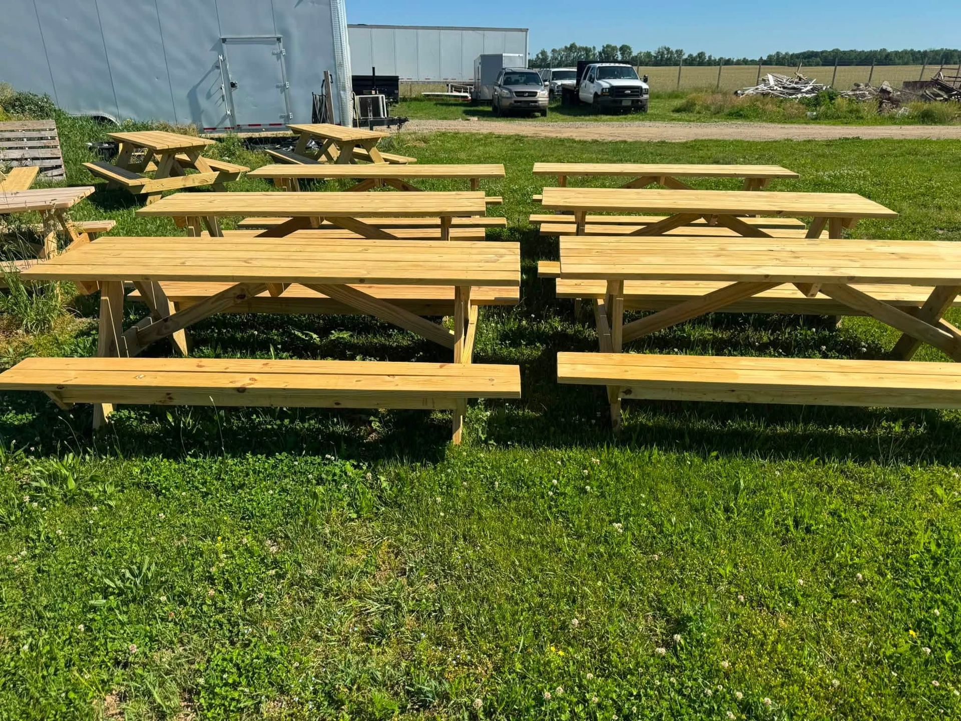 Yellow picnic tables on grass in an outdoor yard near a building and parked vehicles