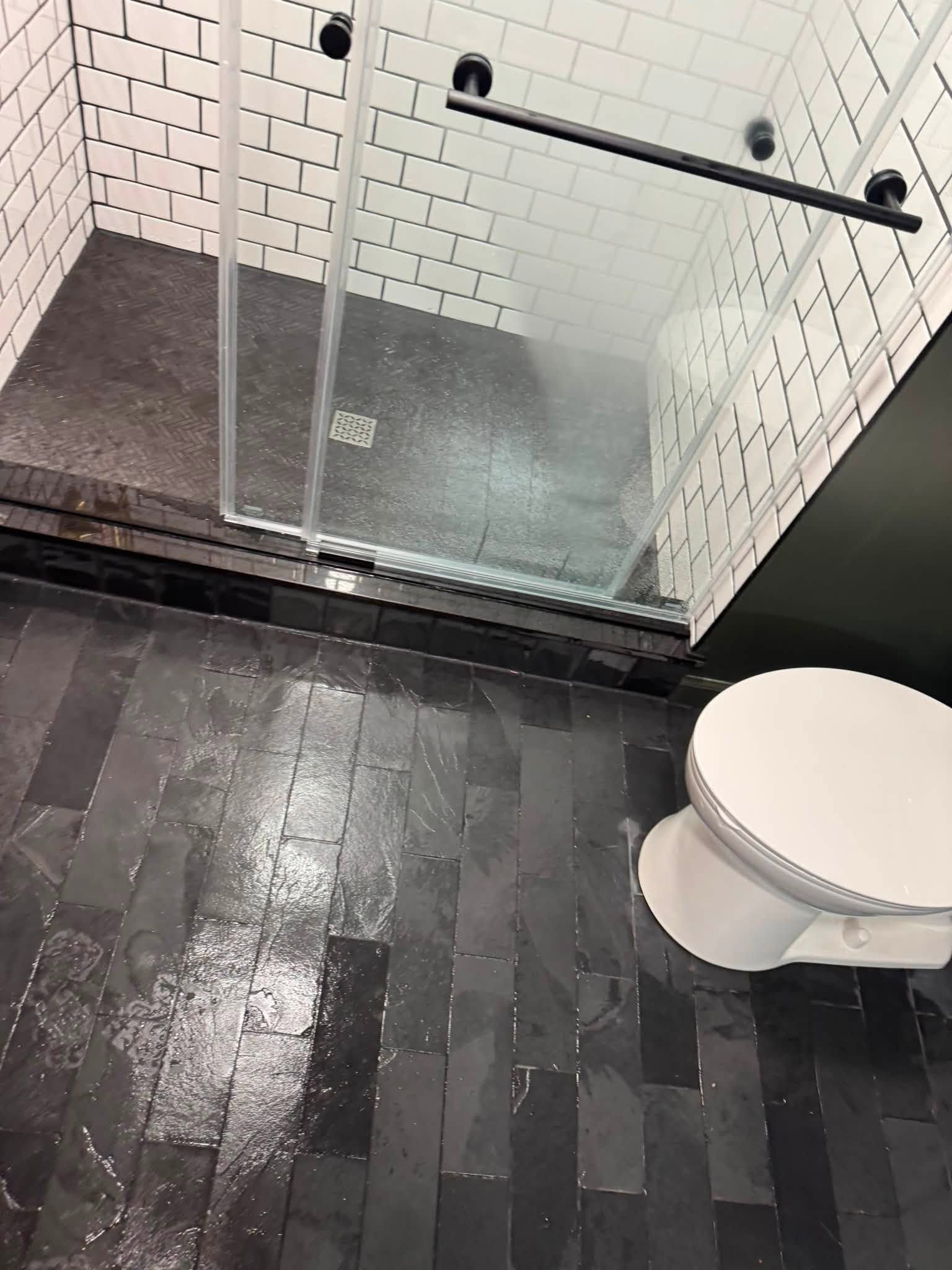Small tiled bathroom with glass shower enclosure, dark floor, and white toilet.