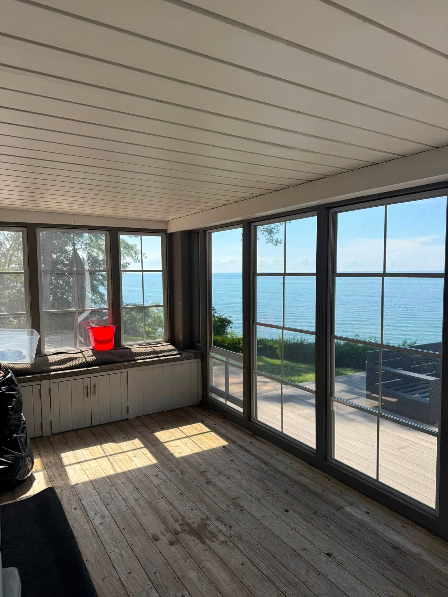 Sunlit room with large windows overlooking the ocean and a red bucket on the counter
