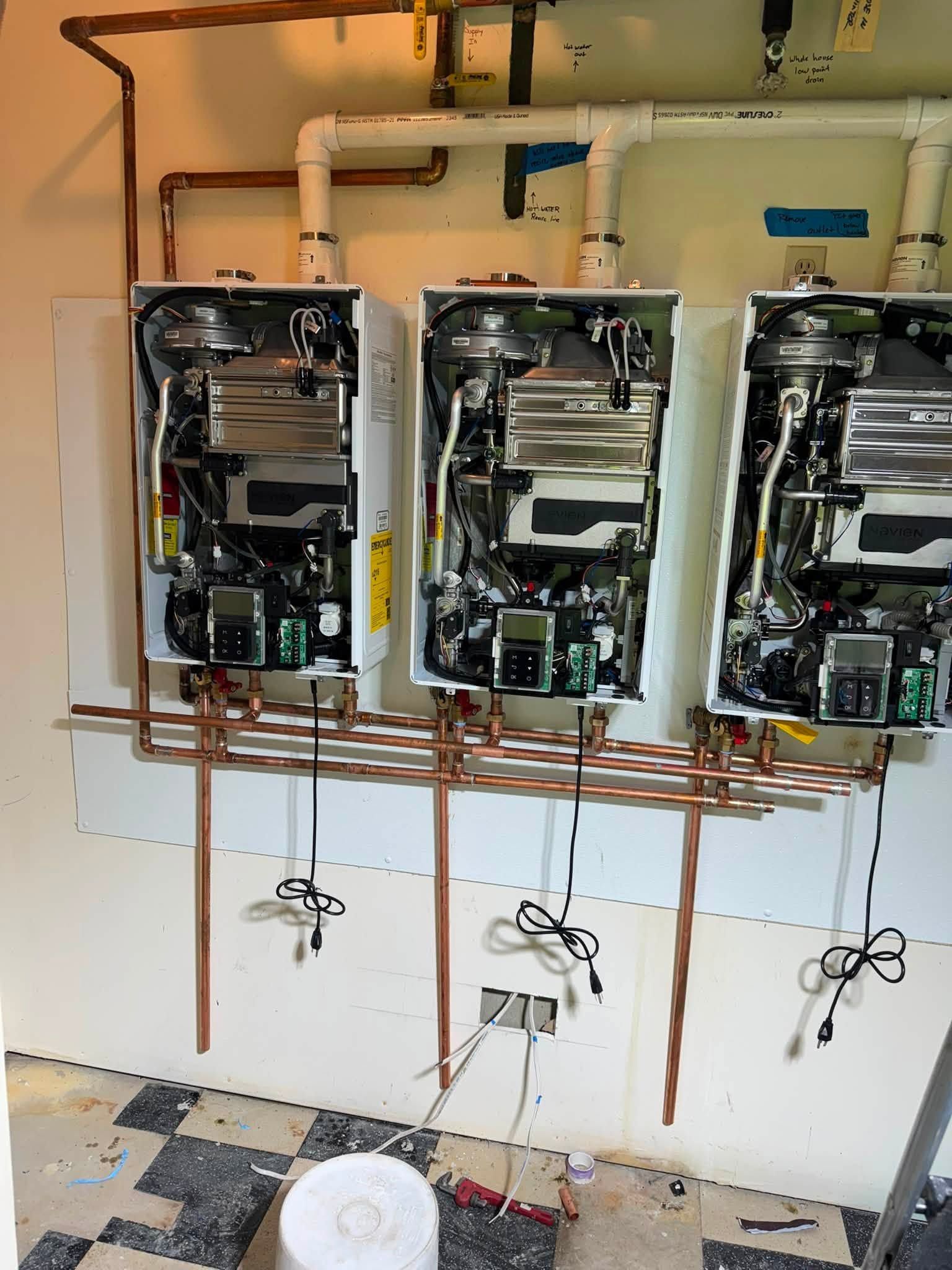 Three open wall-mounted water heaters with exposed copper pipes in a utility room, one showing blue tape.