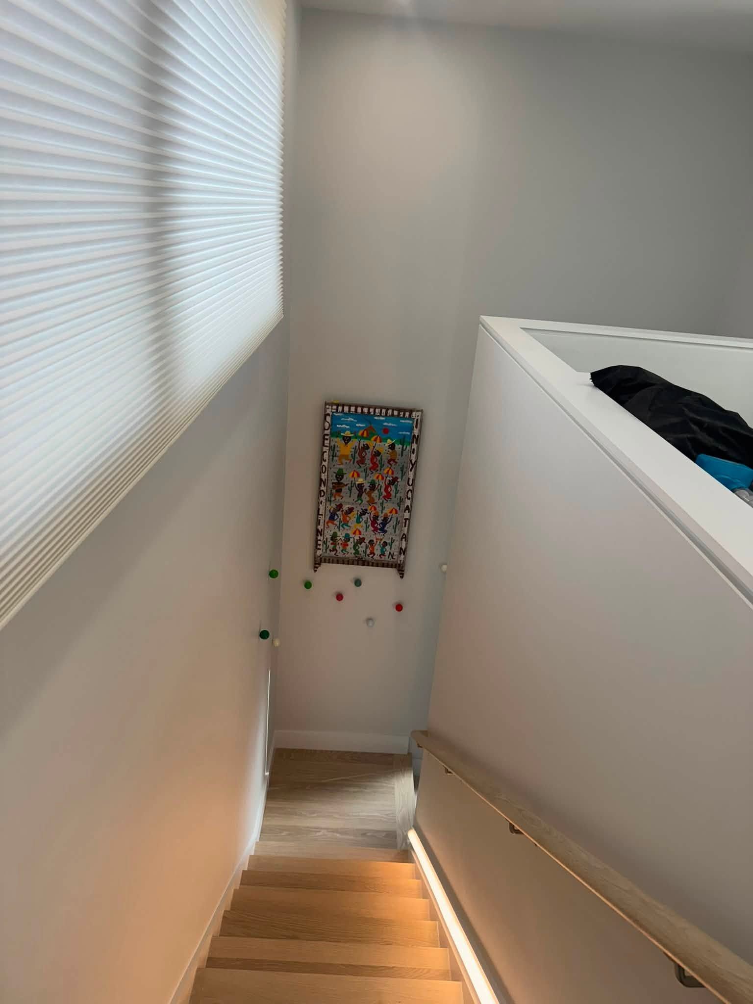 Narrow stairwell with a wall-mounted dartboard, white walls, and daylight from a window blind.