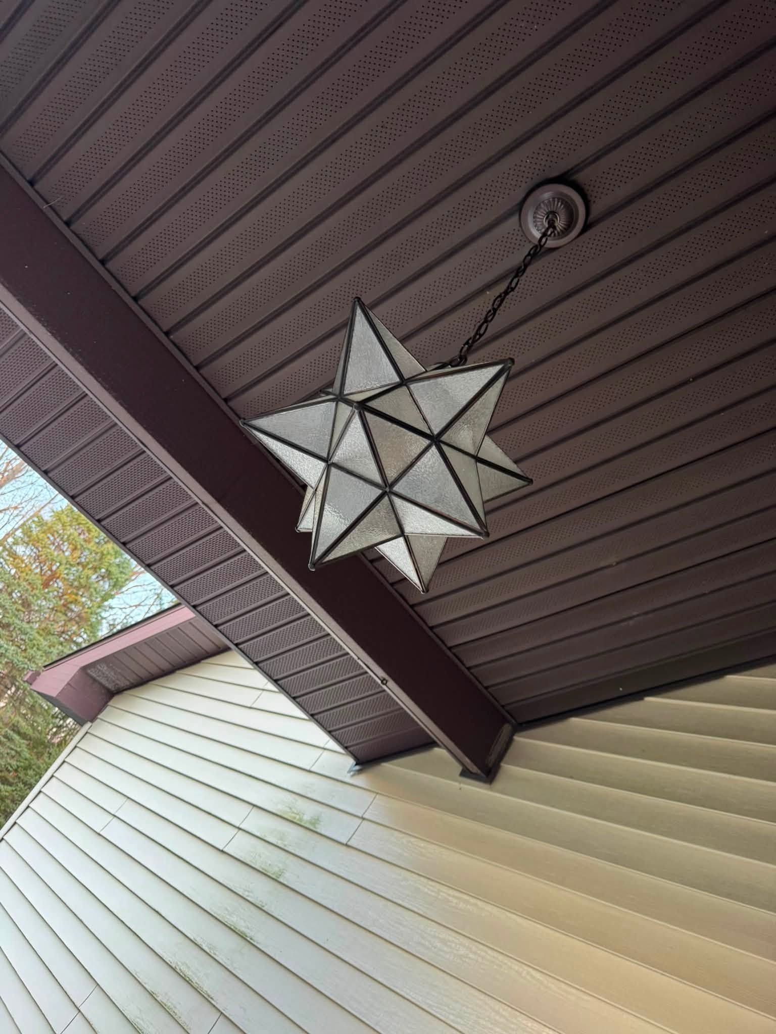 Geometric star lantern hanging from a brown porch ceiling above cream siding.