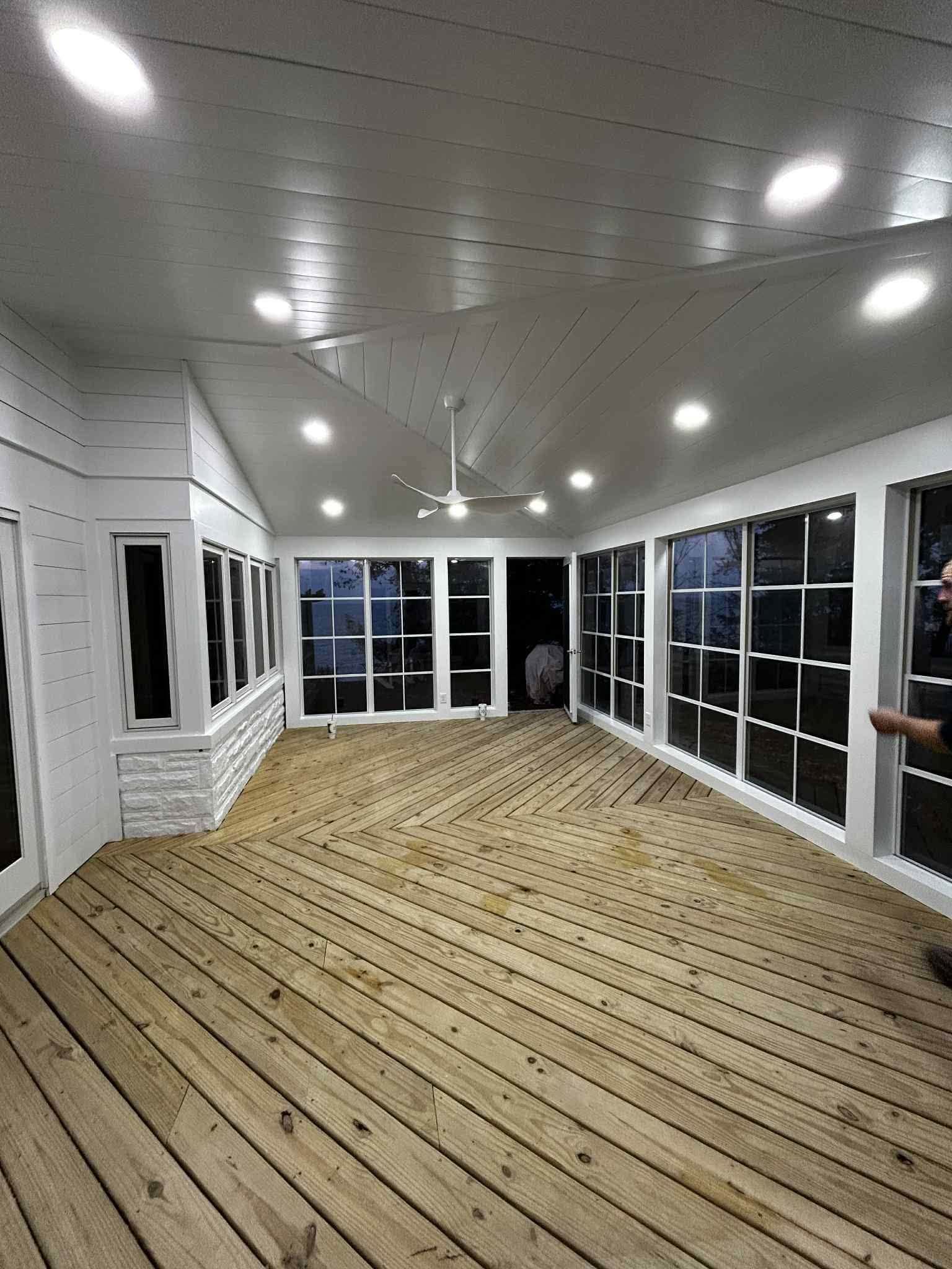Covered porch with wooden floor, white ceiling lights, and screened windows at dusk