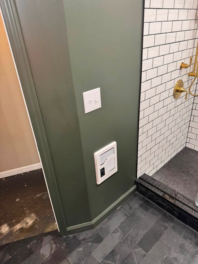 Hallway corner with olive wall, light switch, vent, tiled shower wall, and dark floor tiles.