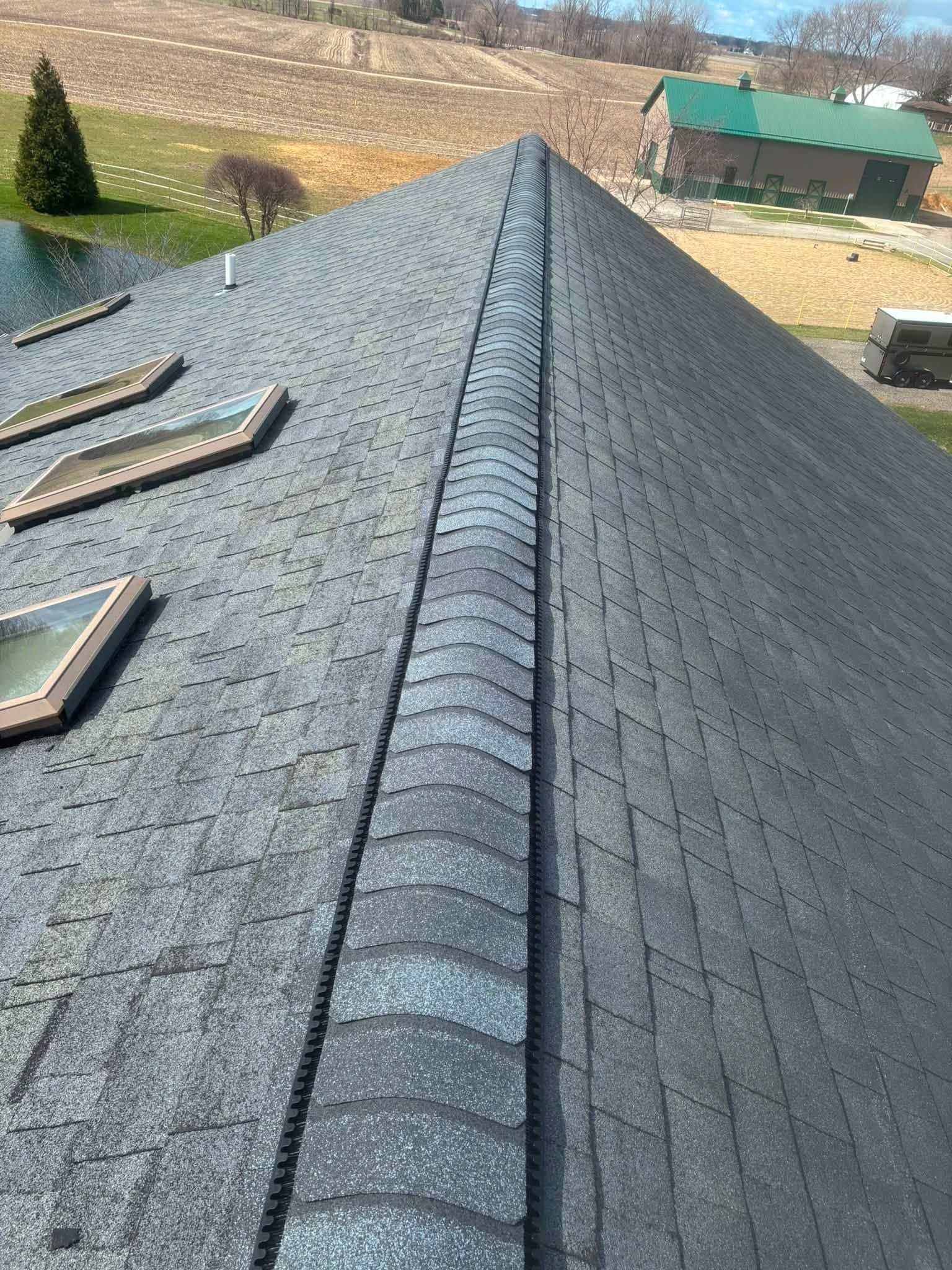 Roof ridge with gray shingles on a house, viewed from above on a sunny day.