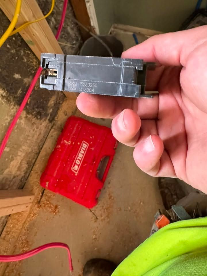 Hand holding a black electrical breaker near a red toolbox on a dirty floor
