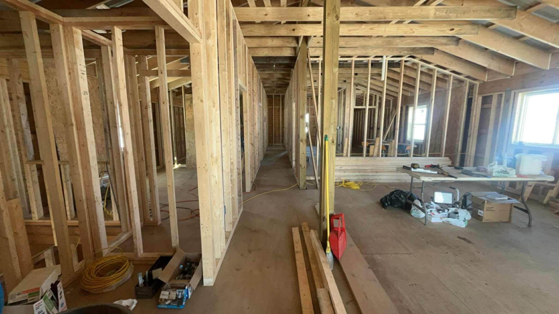 Unfinished house interior with exposed wooden framing, open rooms, and construction materials scattered on the floor