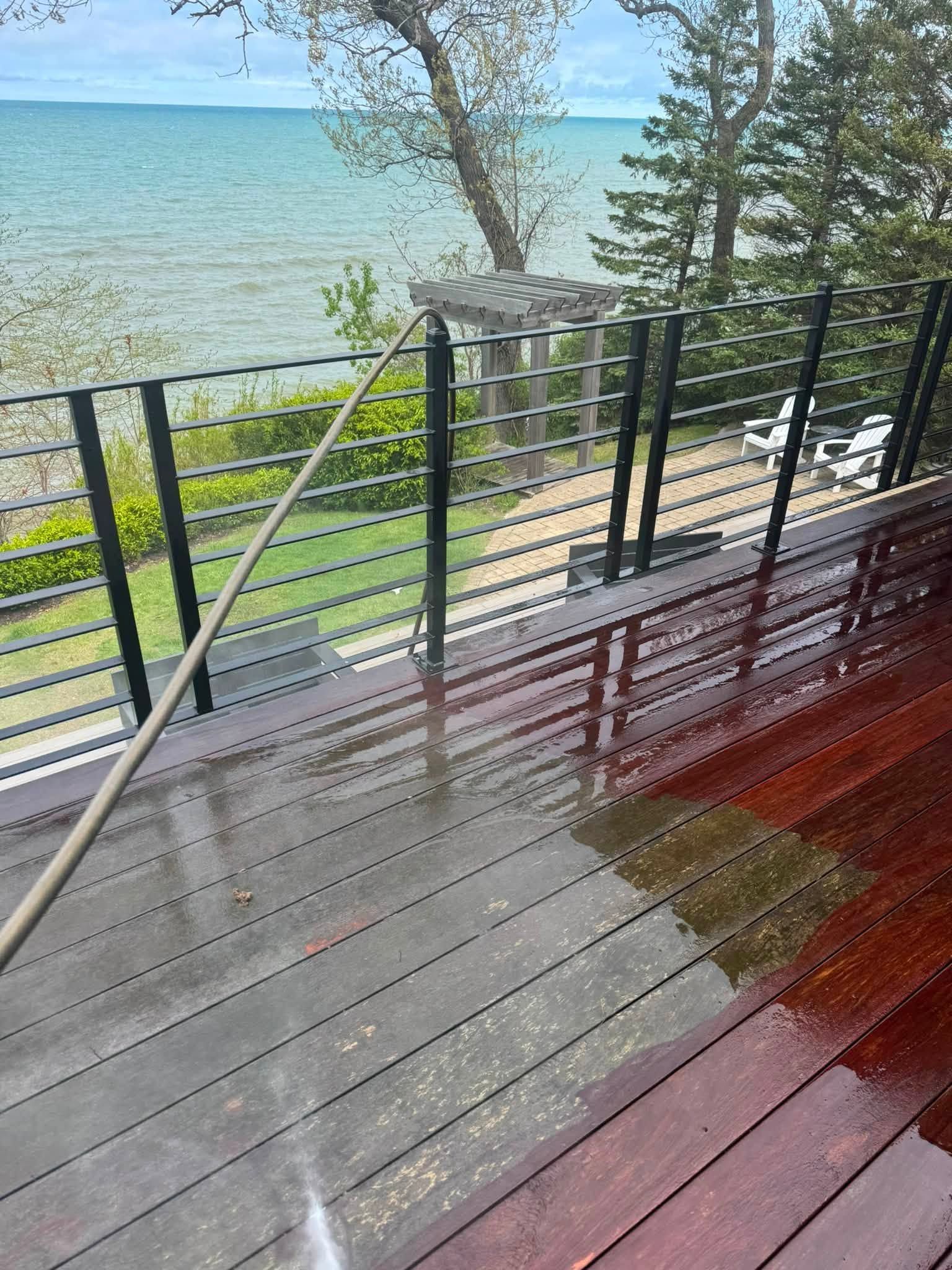 Wet wooden deck with black railing overlooking a lake and trees on a cloudy day