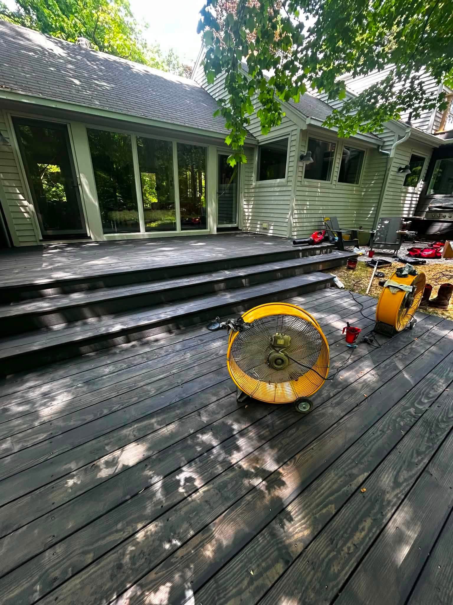 Deck with steps, coiled yellow hose, and tools beside a house under trees