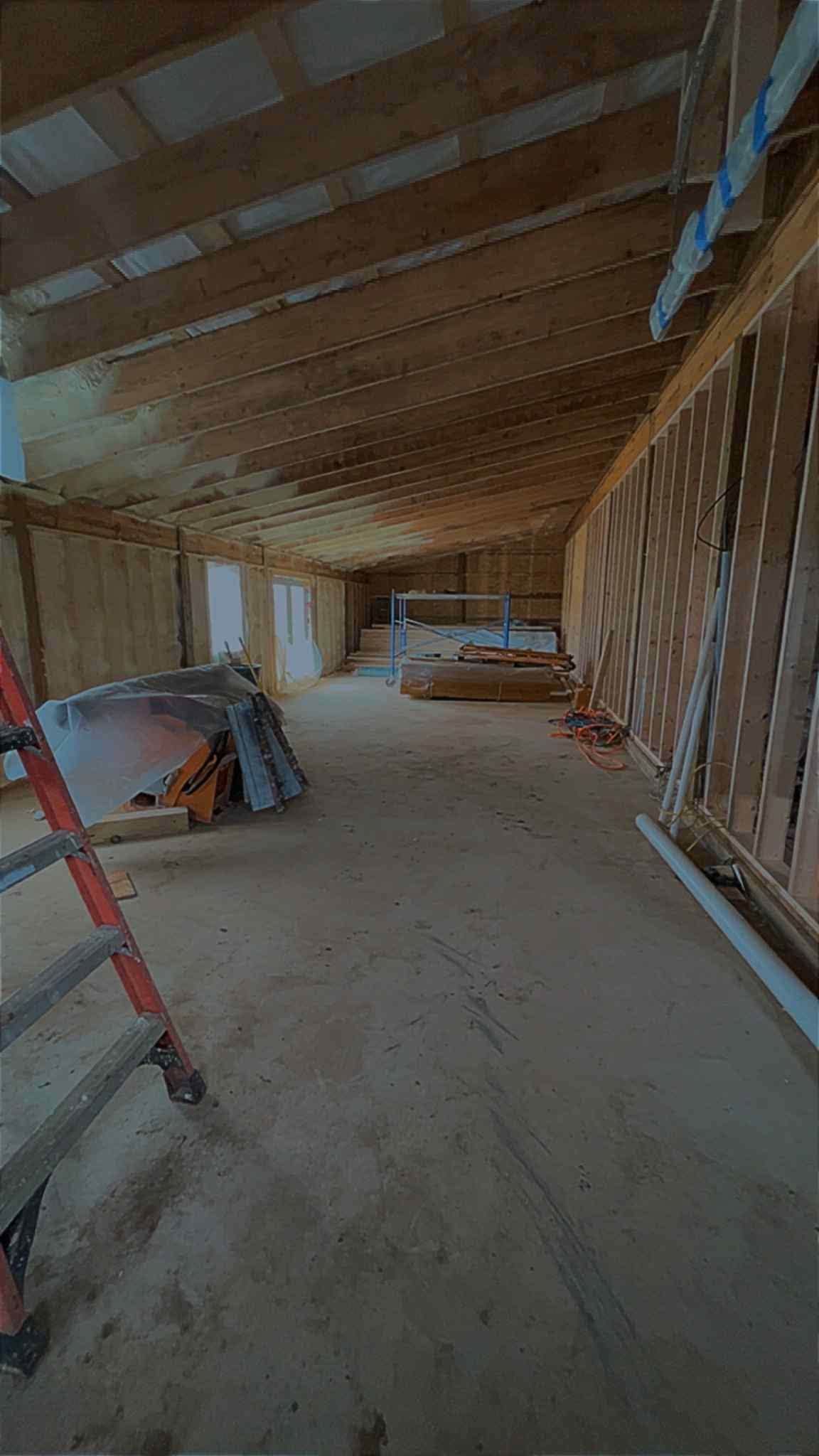 Interior under construction with exposed wooden beams, drywall framing, and tools on a dusty floor.