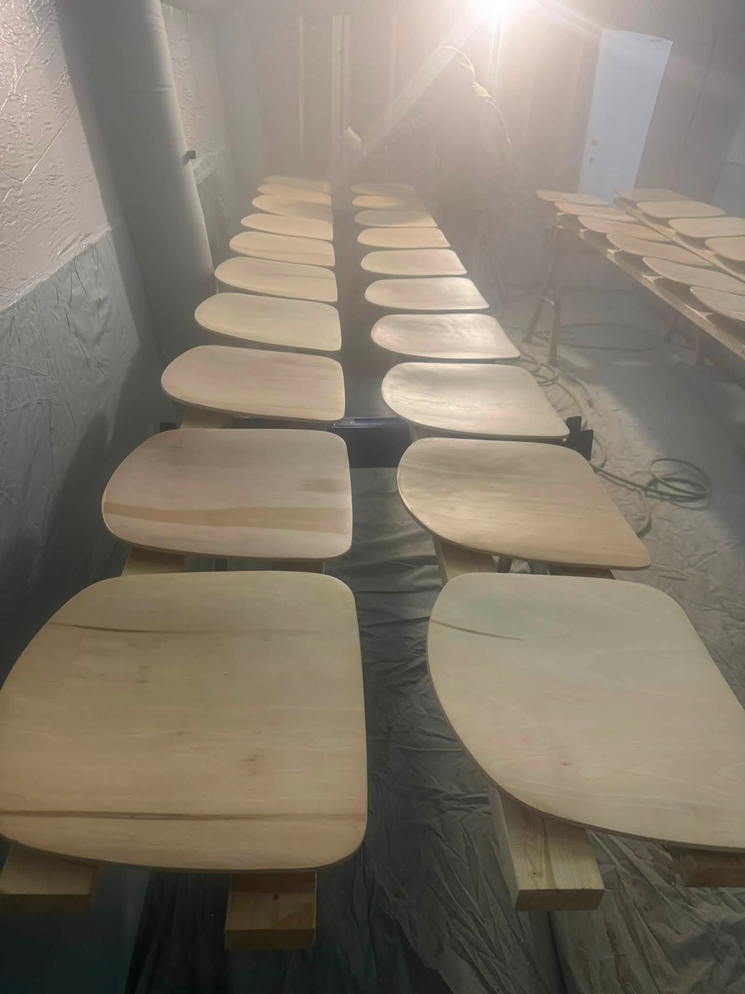 Rows of unfinished wooden trays or boards arranged in a workshop, viewed from a narrow aisle.