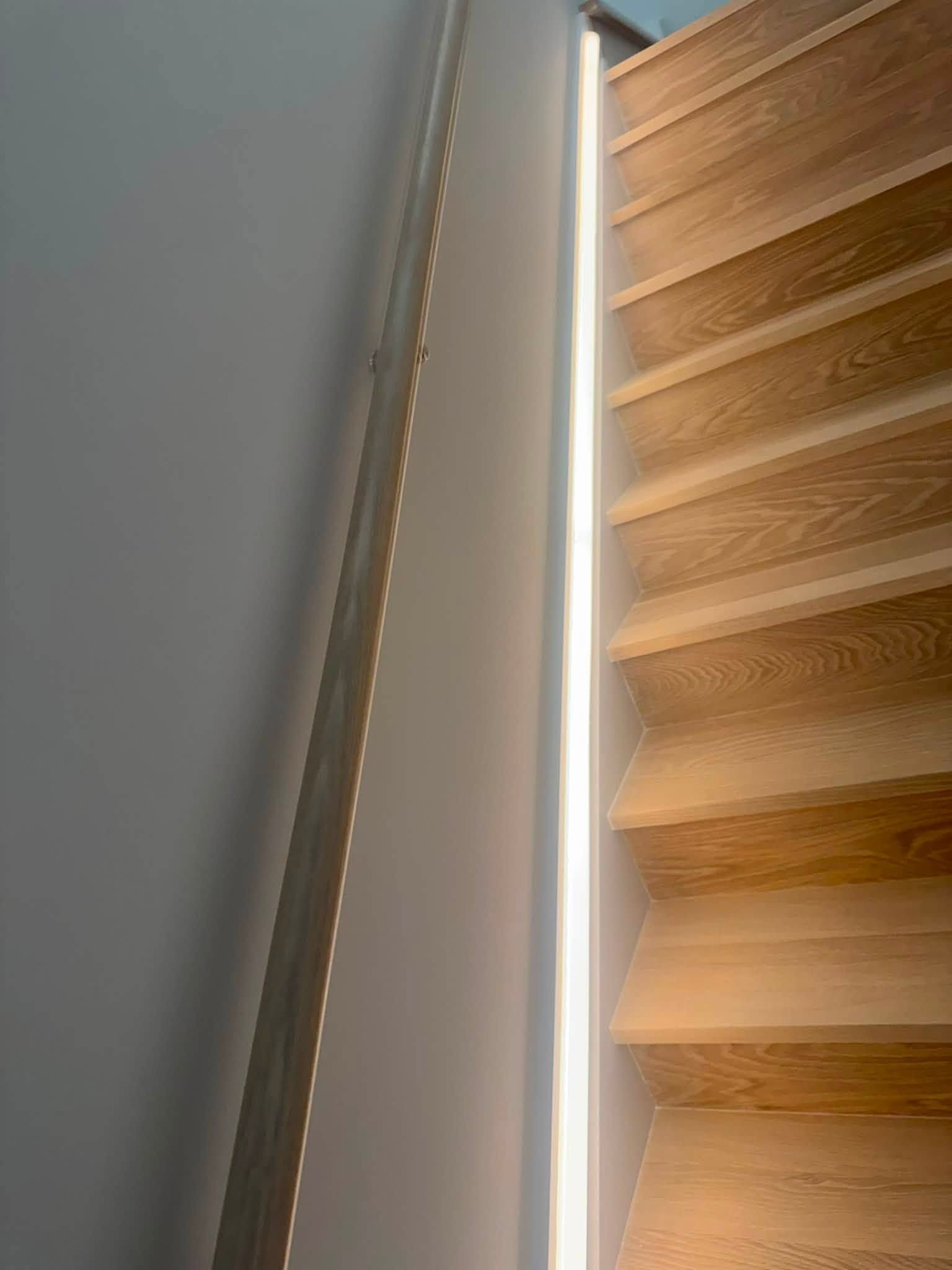 Wooden stairs beside a gray wall with a narrow strip of light between them