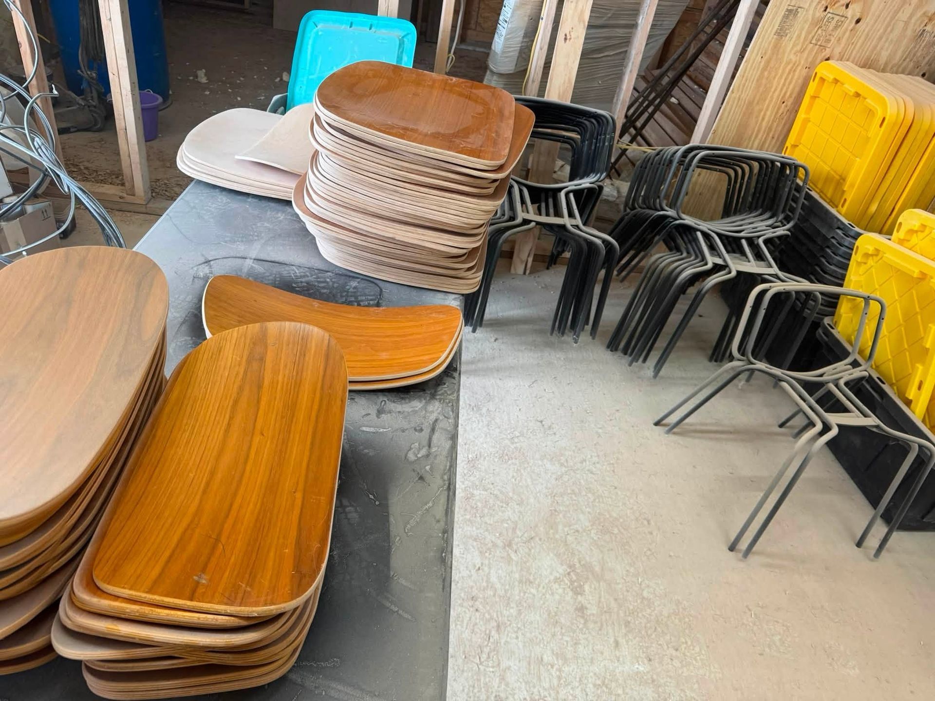Stacked wooden and metal chairs and tabletops stored in a warehouse-like room