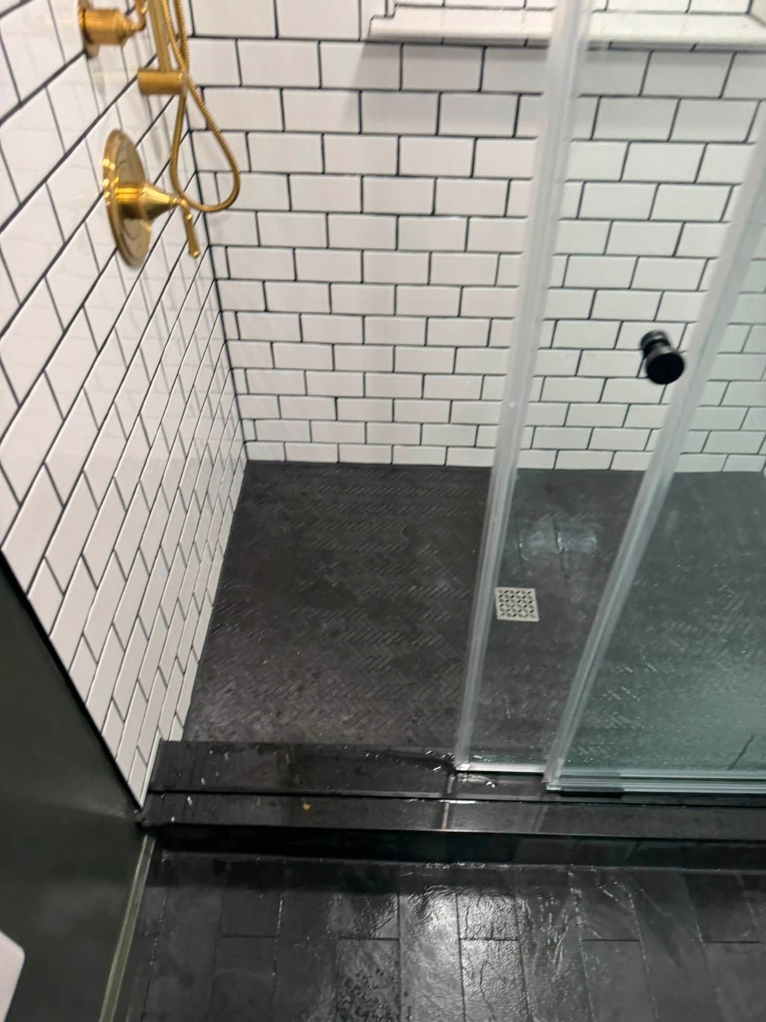 Small tiled shower stall with glass door, dark floor, and wall-mounted showerhead.