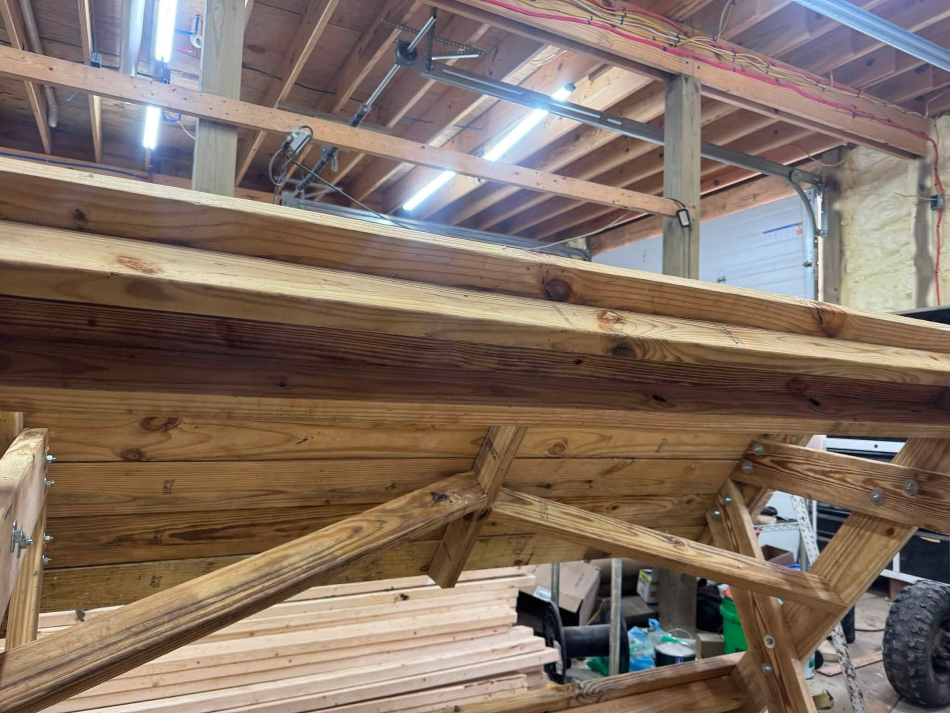 Wooden boat hull under construction inside a workshop, with exposed rafters and tools in the background
