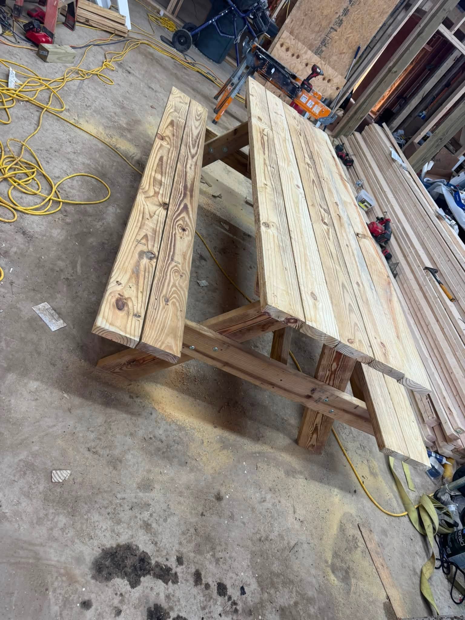 Wooden workbench with long planks in a cluttered workshop, surrounded by coiled extension cords and tools.