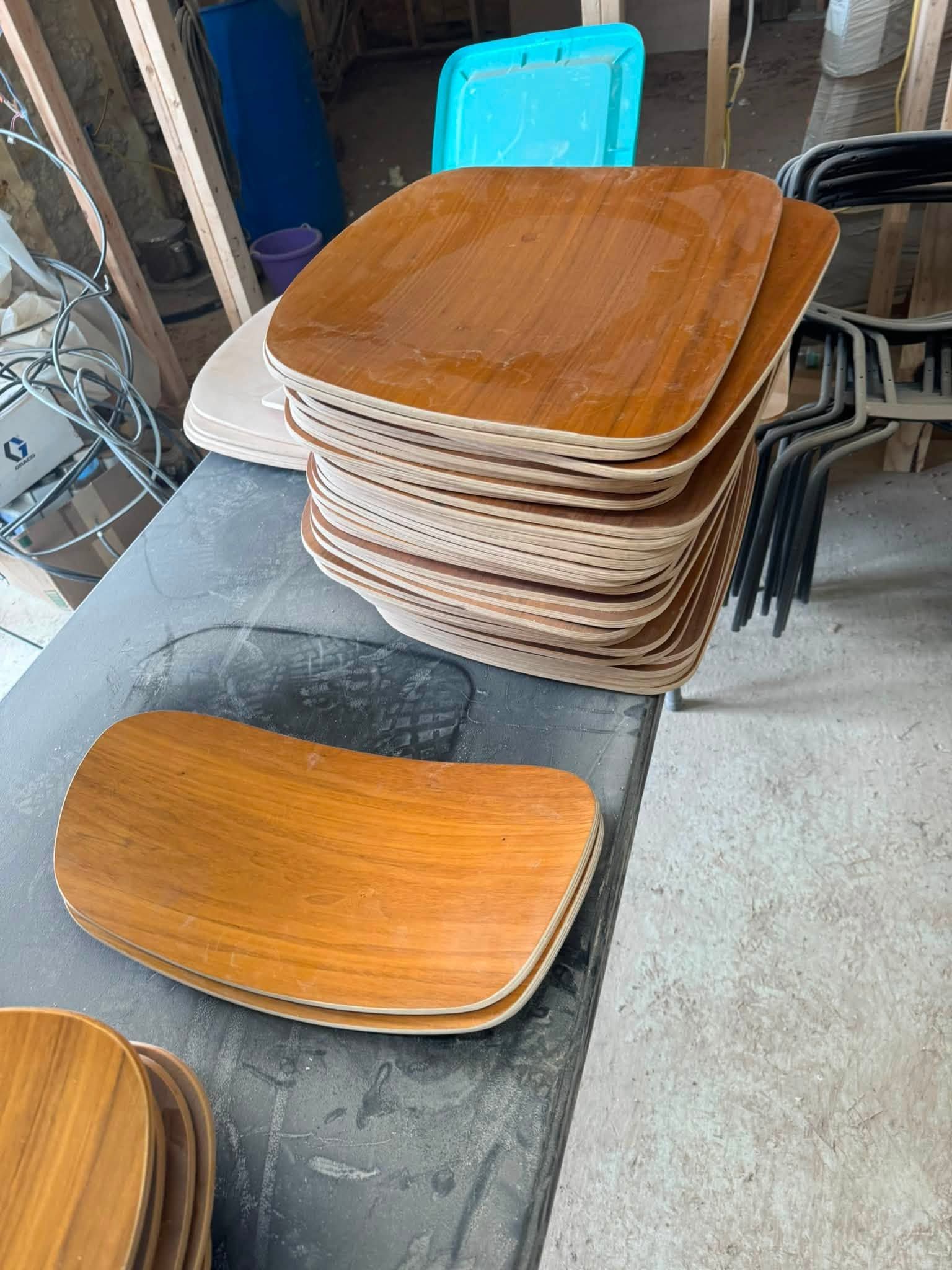 Stacked wooden chair seat pads on a gray surface in a workshop or storage area.