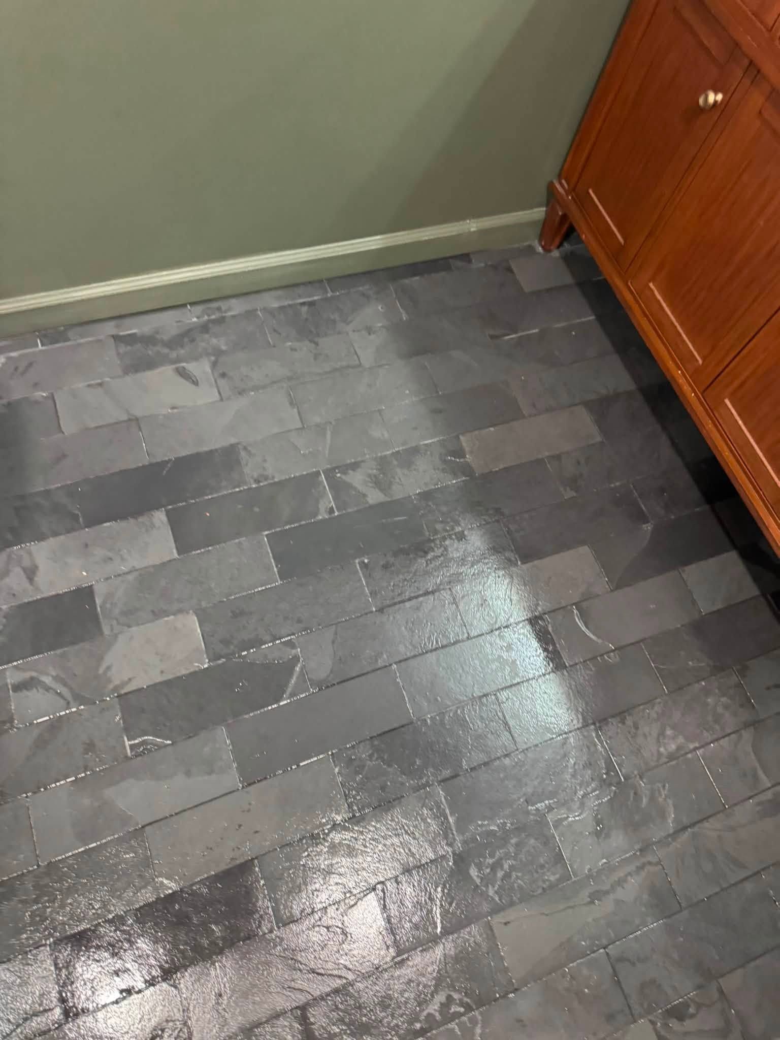 Wet gray tiled floor beside a wooden cabinet in a kitchen corner