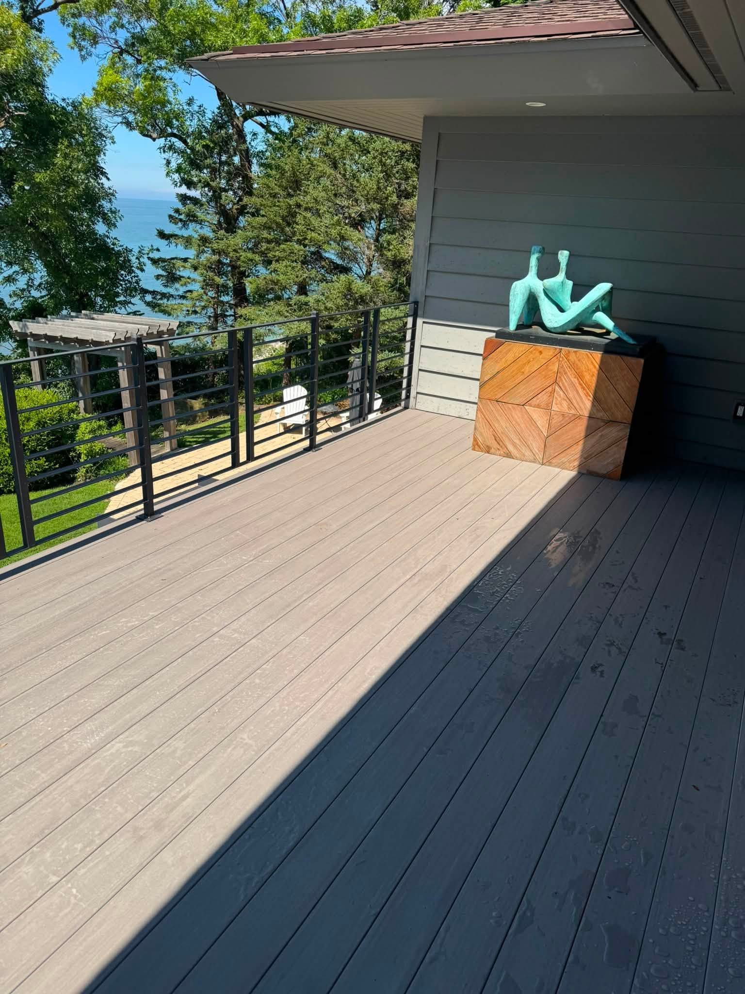 Sunny deck with black railing, gray siding, and turquoise chairs beside a wooden planter box.