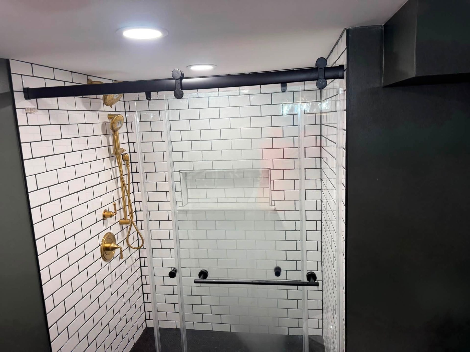 Modern shower stall with white subway tiles, glass doors, black fixtures, and gold shower controls.