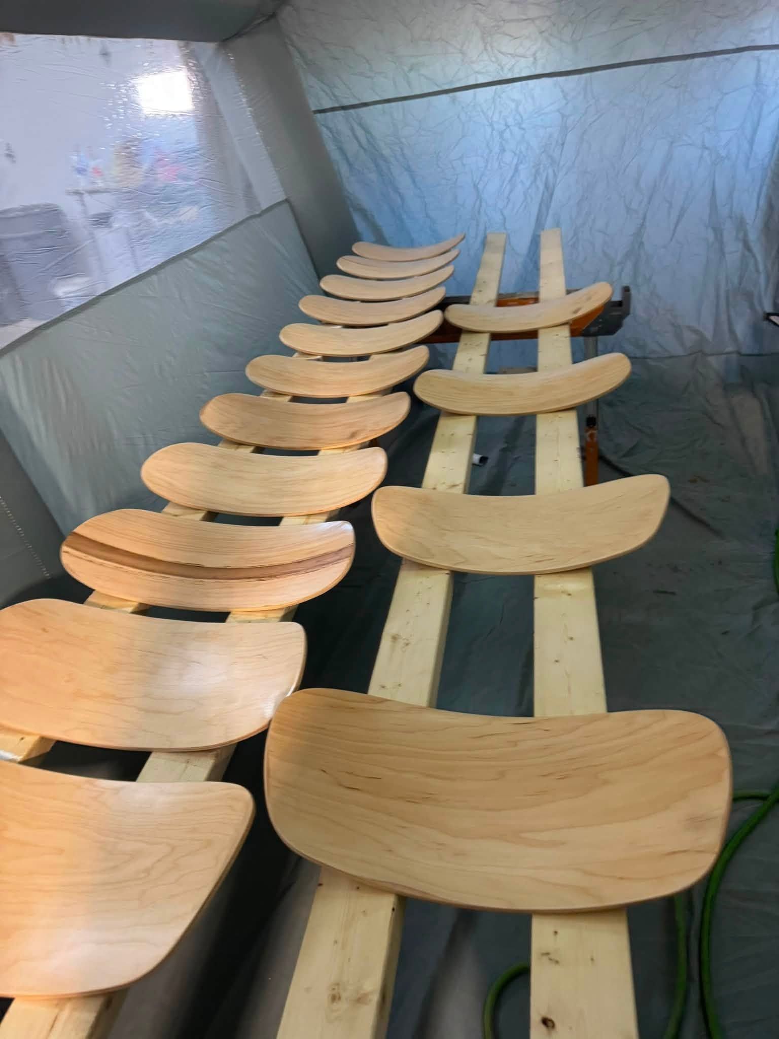 Rows of curved wooden seats in a bright, unfinished room or installation space