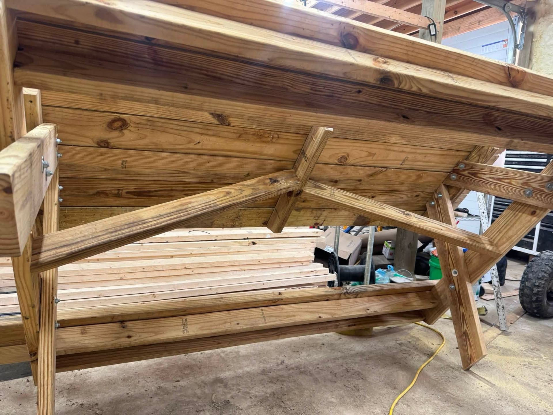 Wooden workbench with angled braces in a workshop, unfinished wood slats and a yellow extension cord nearby