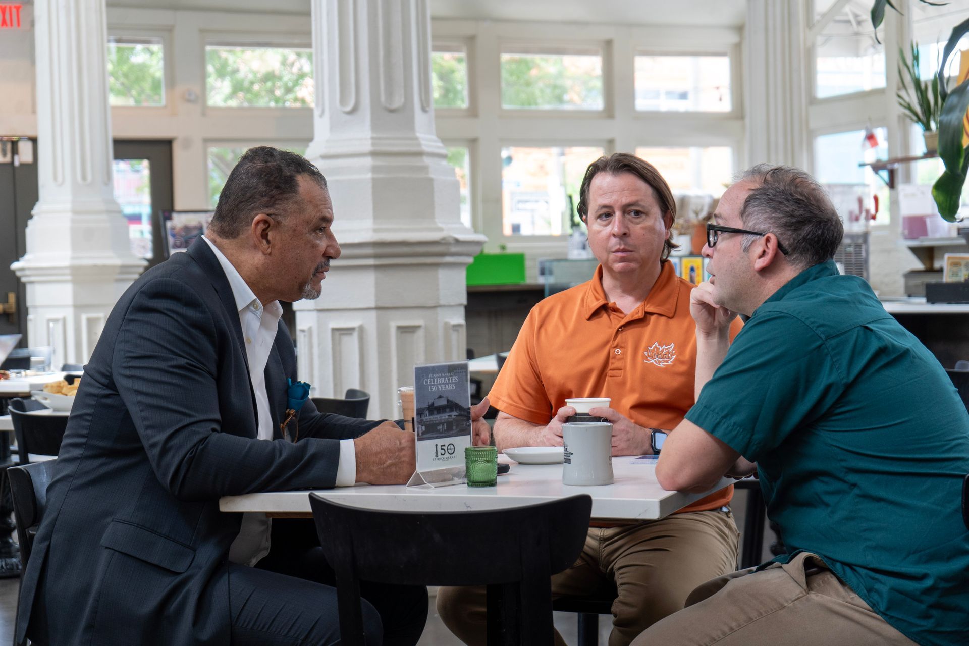Oliver Thomas in a suit and tie is leaning against a wall.