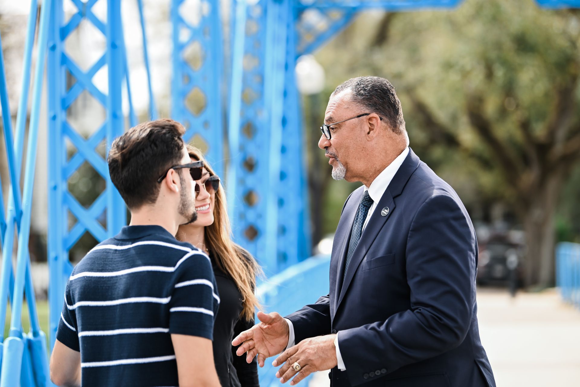 Oliver Thomas in a suit and tie is talking to two people on a bridge.