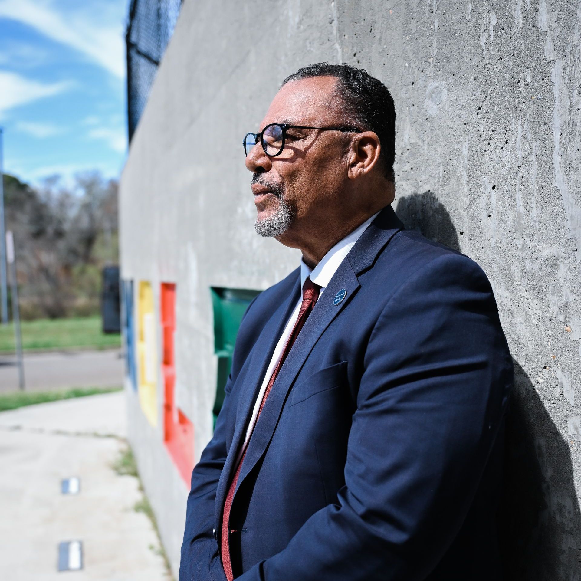 Oliver Thomas in a suit and tie is leaning against a wall.