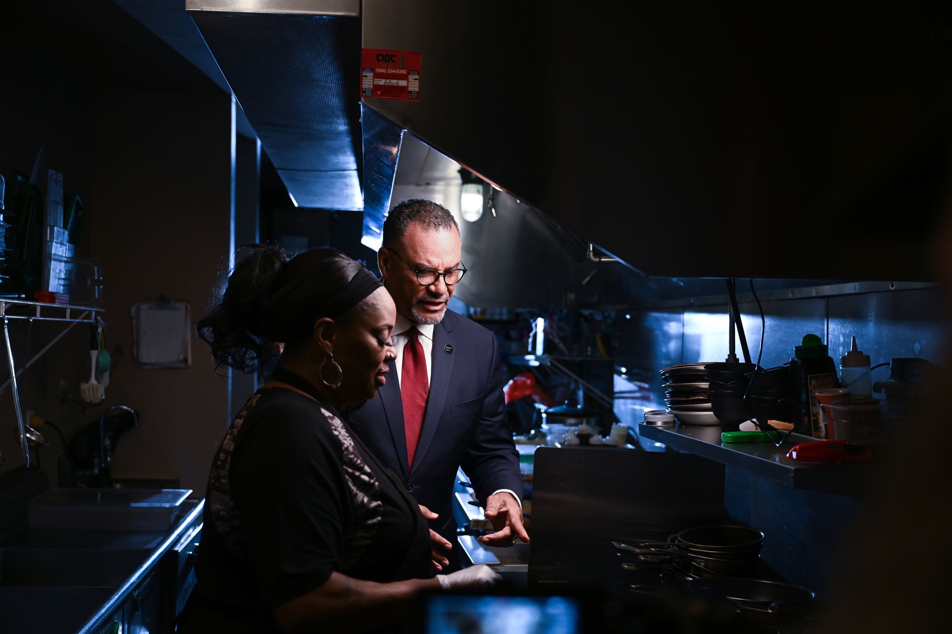 Oliver Thomas in a suit and tie is standing next to a woman in a kitchen.
