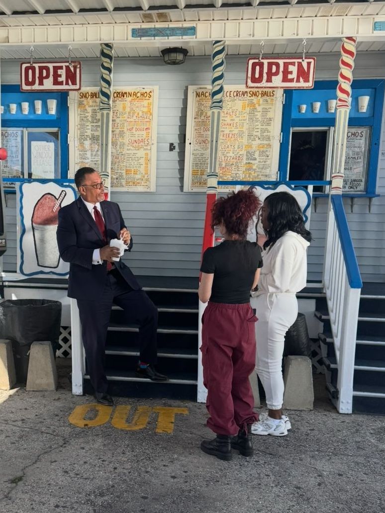 Oliver Thomas in a suit is talking to two women in front of an open sign