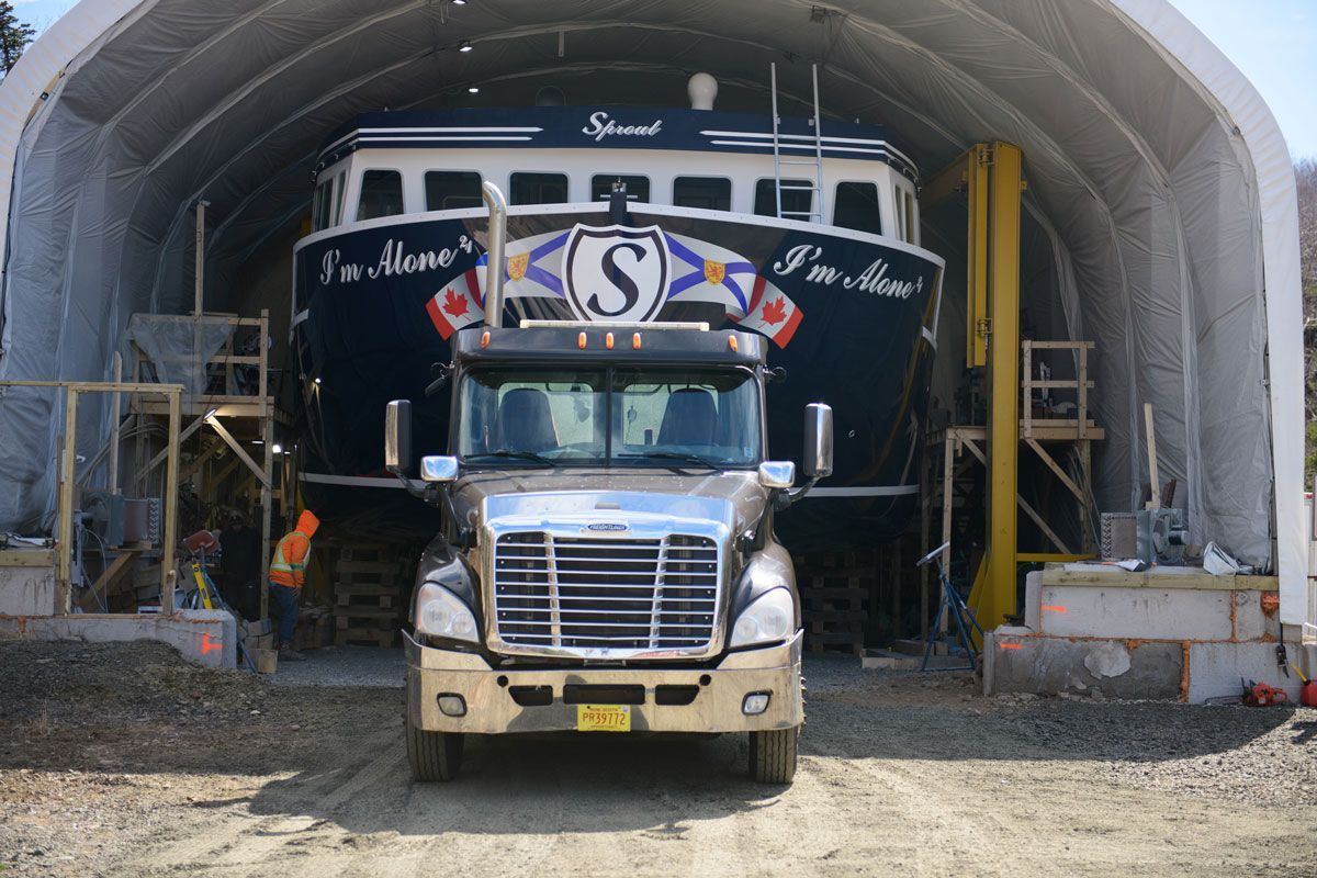 A truck is parked in front of a boat that has the letter s on it