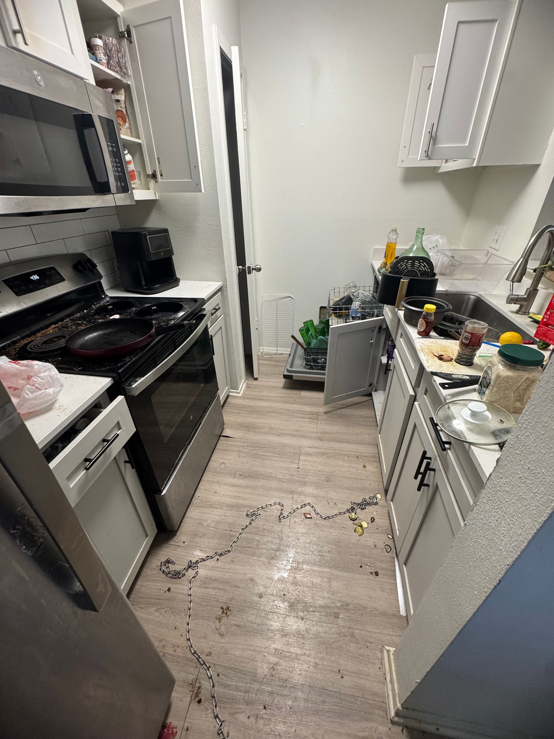 A messy kitchen with a stove, refrigerator, microwave, and sink.