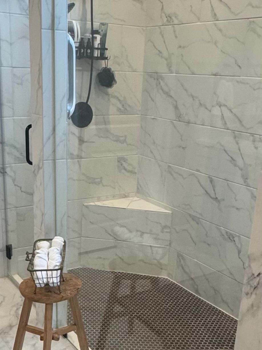 A bathroom with a walk in shower and a stool with towels on it.