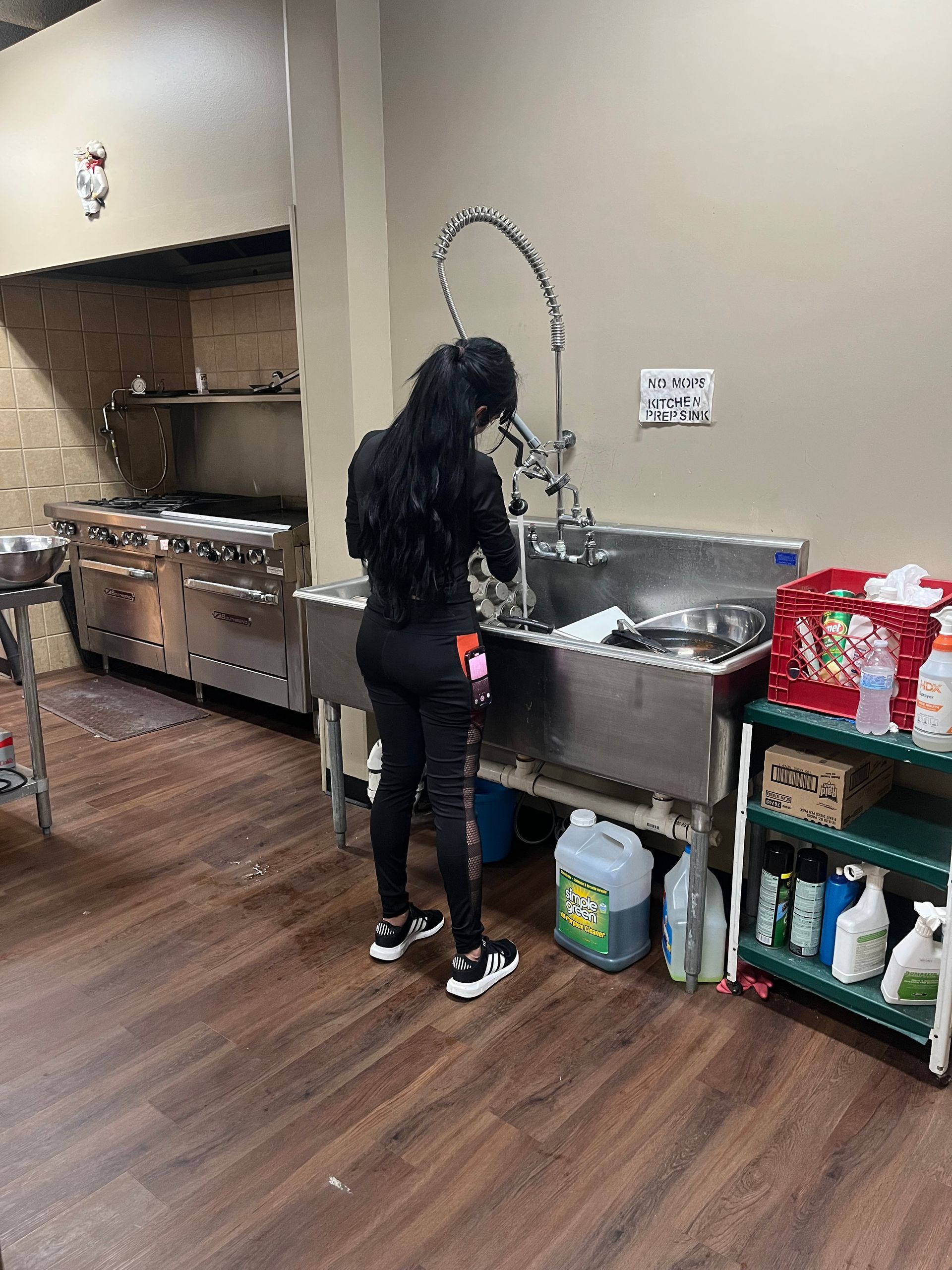 A woman is washing dishes in a kitchen sink.