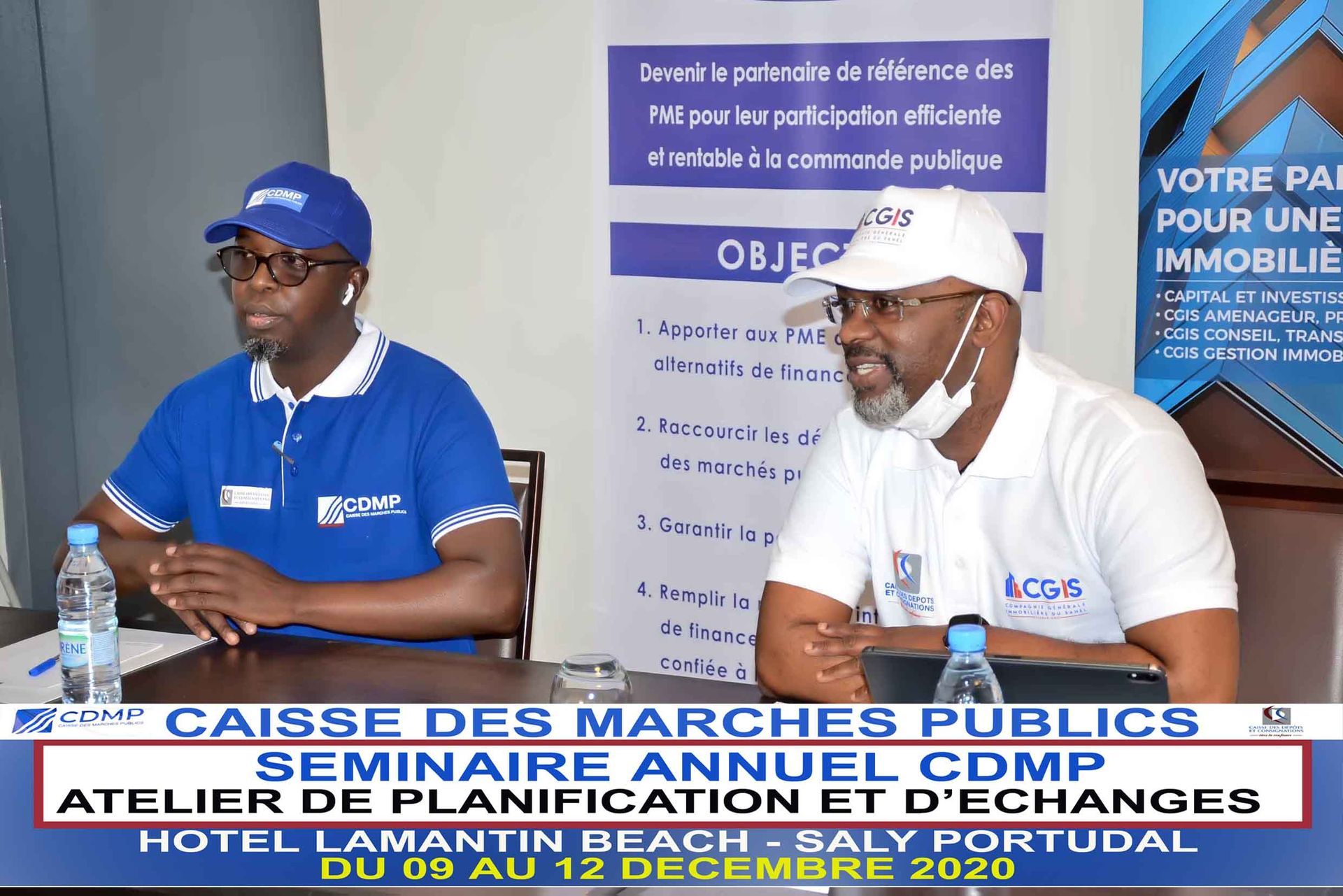 Deux hommes sont assis à une table devant une pancarte indiquant objectif