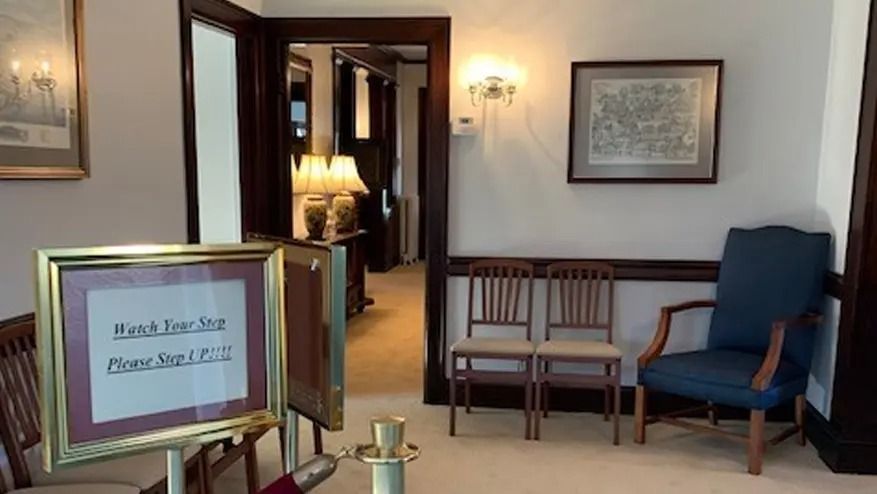 An entryway with a sign, chairs, and a doorway leading to an illuminated room.