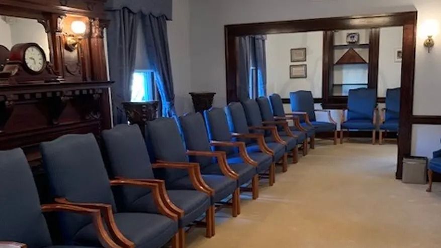 Row of blue chairs in a room with a mirror, dark wood details, and a clock on a mantel.